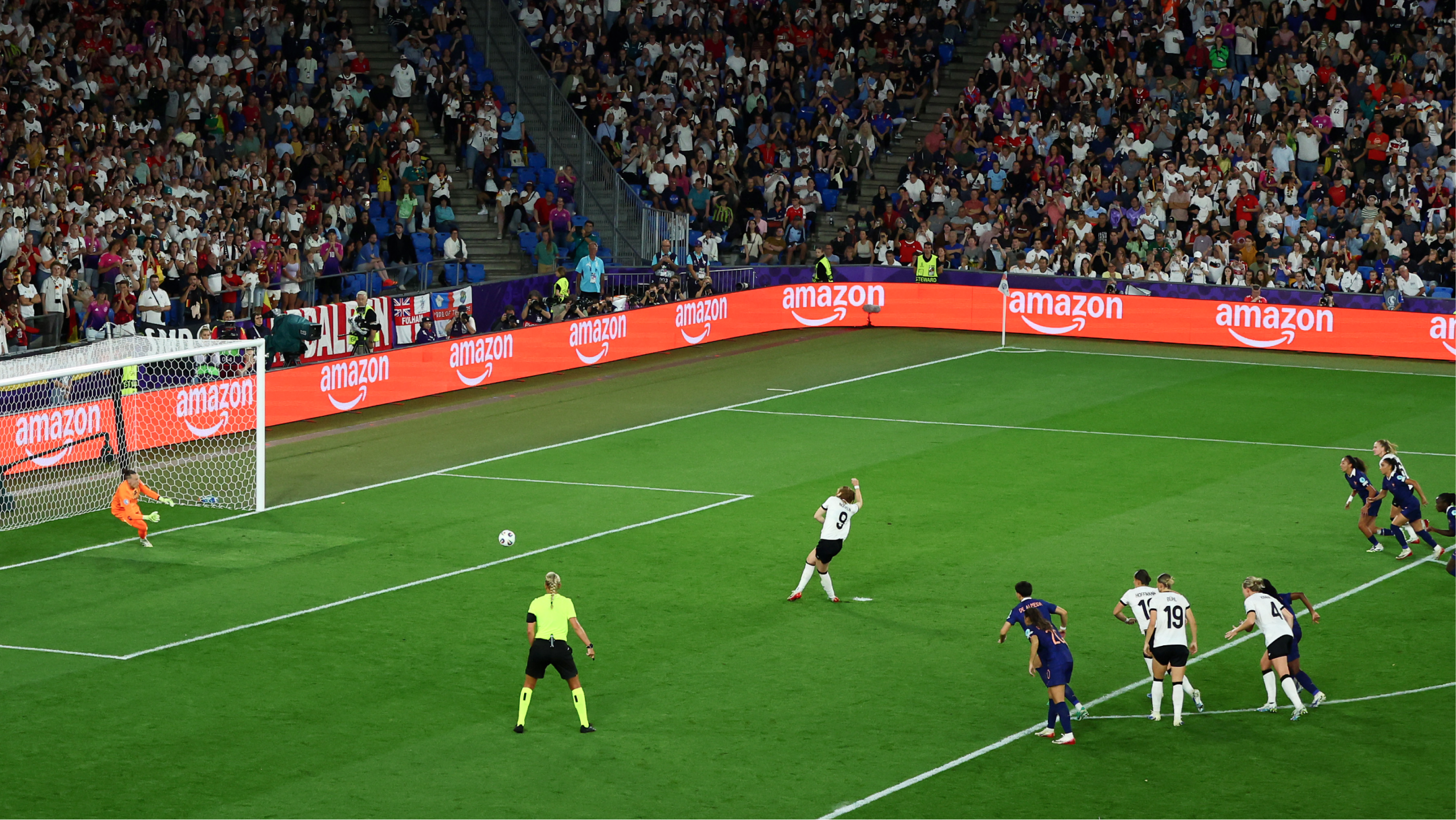 Womens football photo showing a players on the pitch with orange, Amazon branding at the edge of the pitch