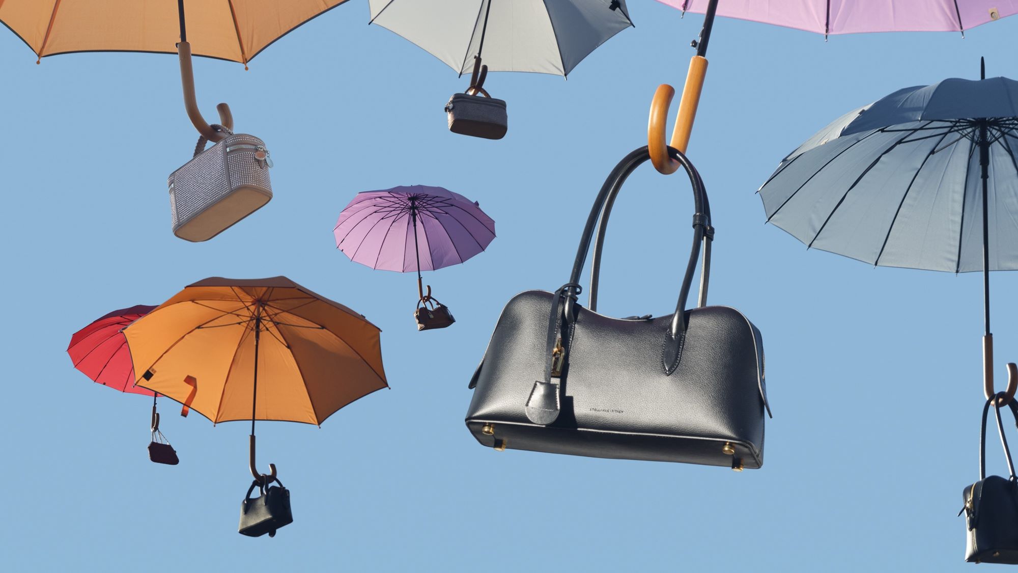 Colorful umbrellas and handbags floating against blue sky