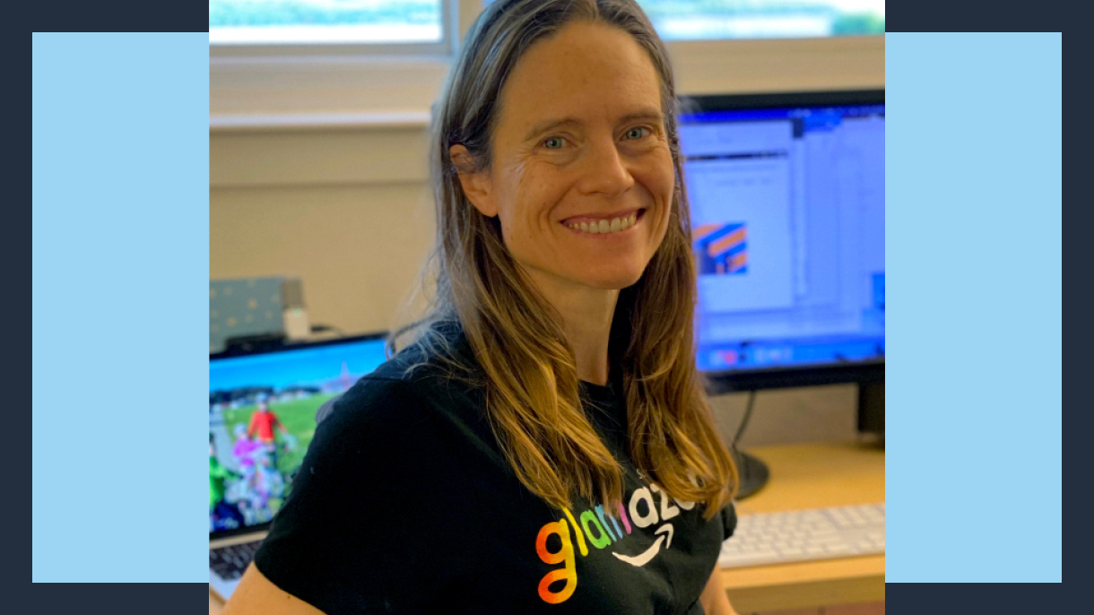 Amazon robotics employee Heidi smiles as she sits at her desk wearing a glamazon shirt.