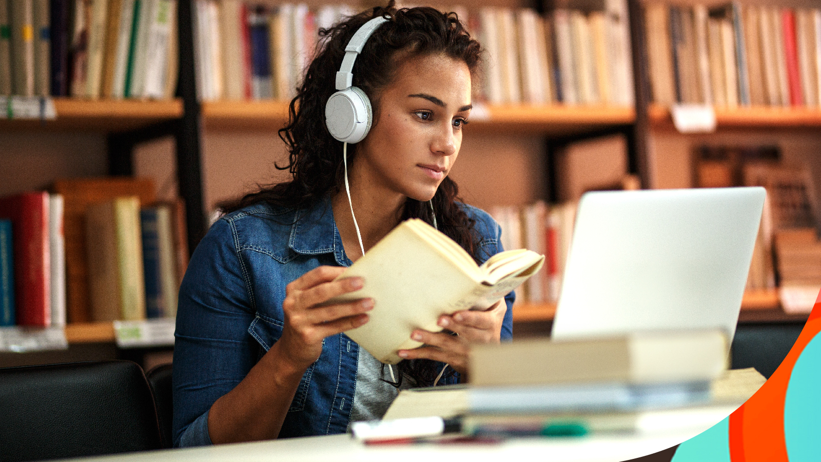 A student wearing headphones and working at a desk in a library