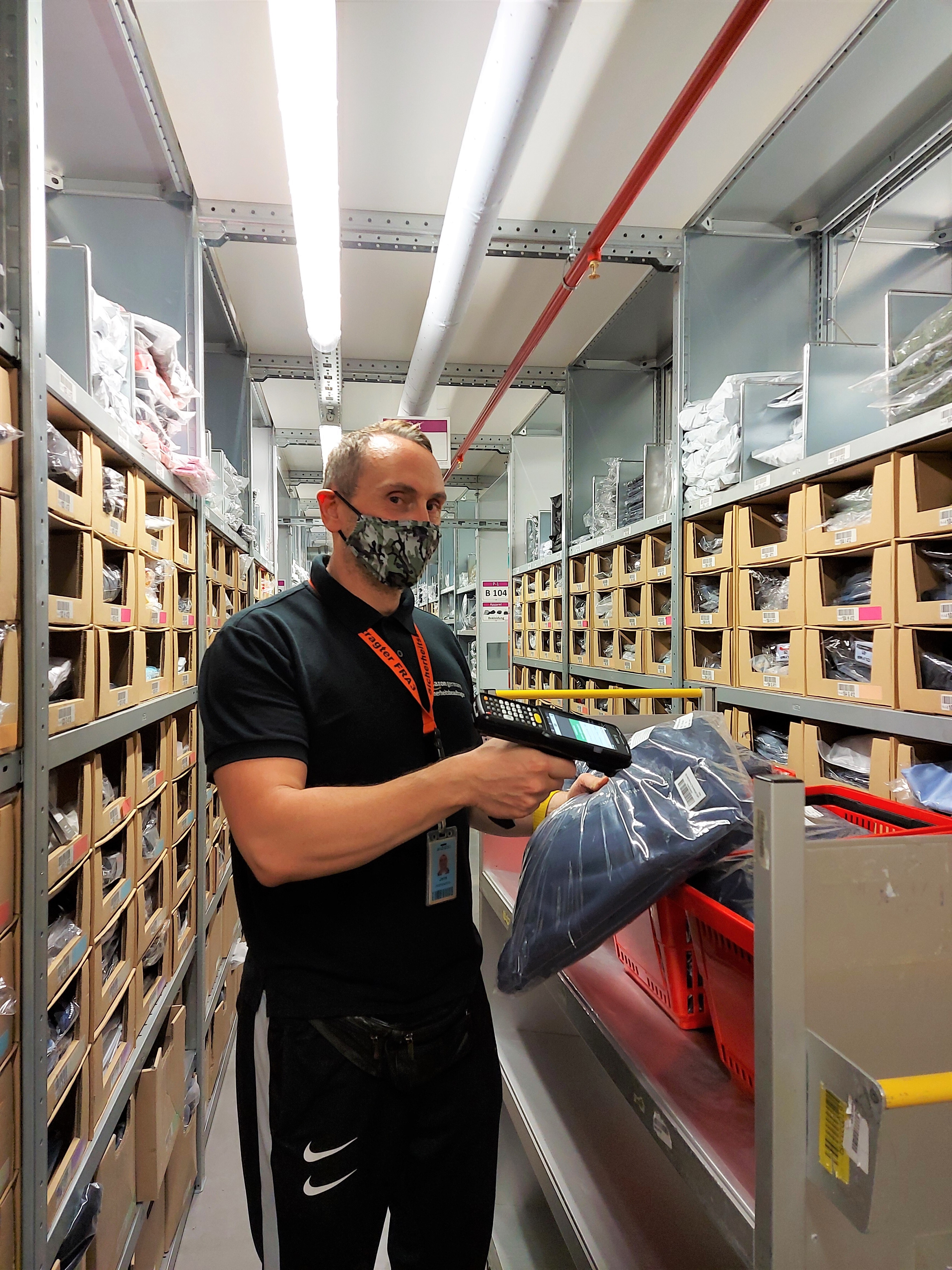 Jens mit schwarzem Poloshirt und Nike-Sporthose sowie in Maske beim Einlagern im Logistikzentrum.