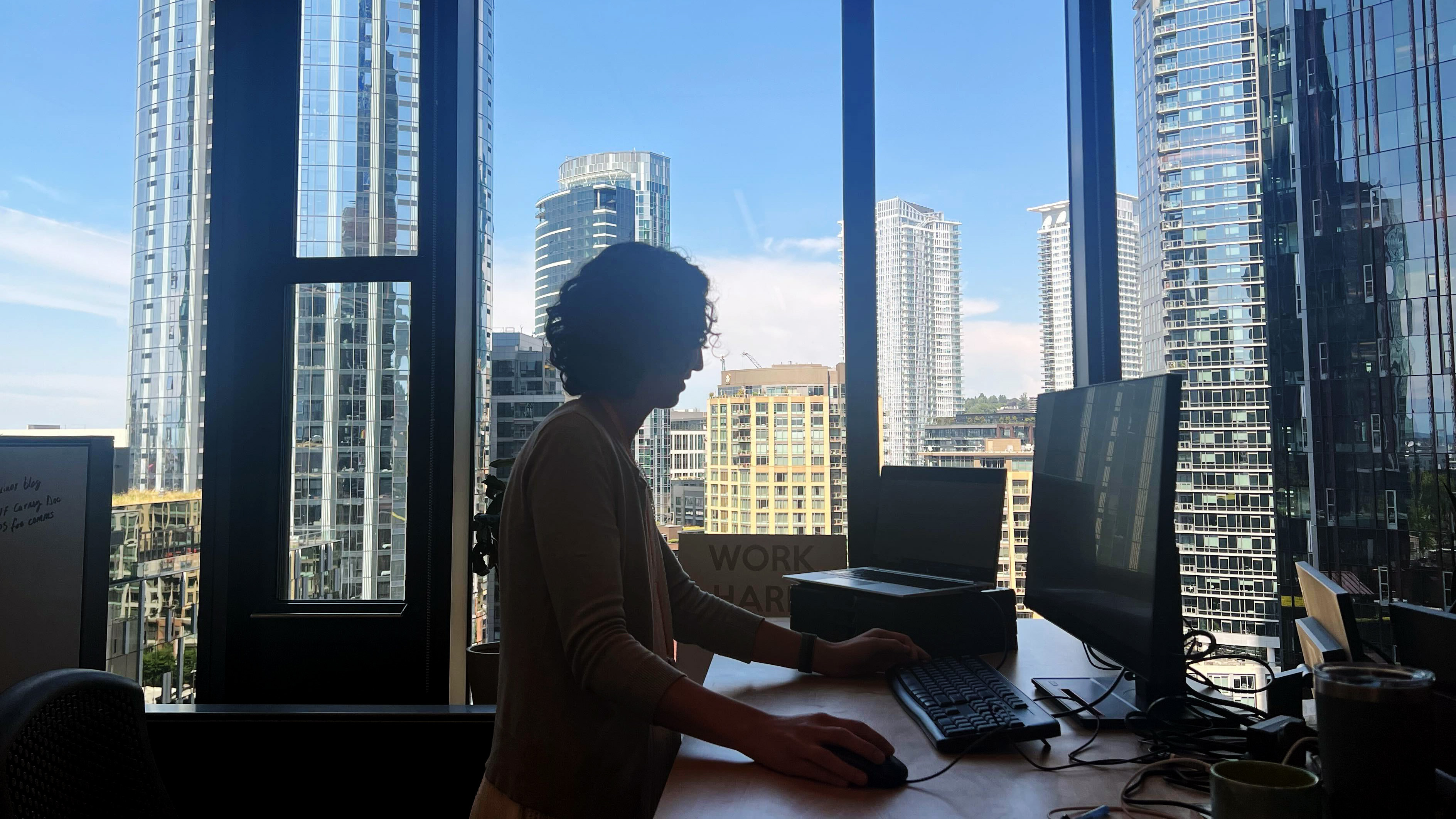 Amazon employee working at her desk with a vivid view of downtown Seattle behind her.