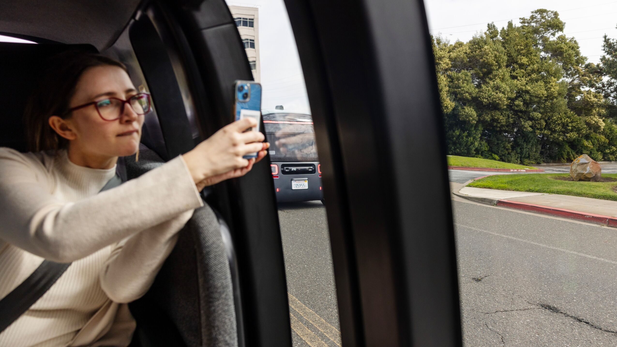 A woman is riding in a Zoox robotaxi, looking out the window and using her phone to photograph what's outside.