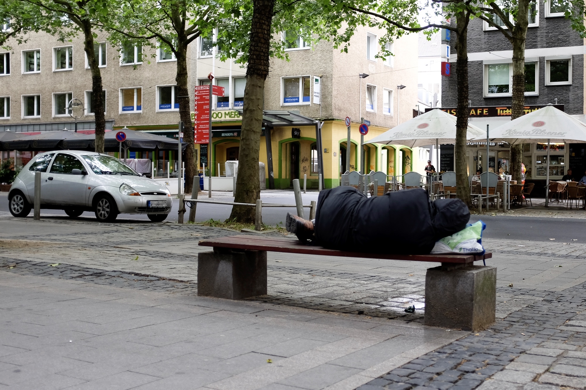 Ein obdachloser Mann ist von hinten auf einer Parkbank liegend zu sehen