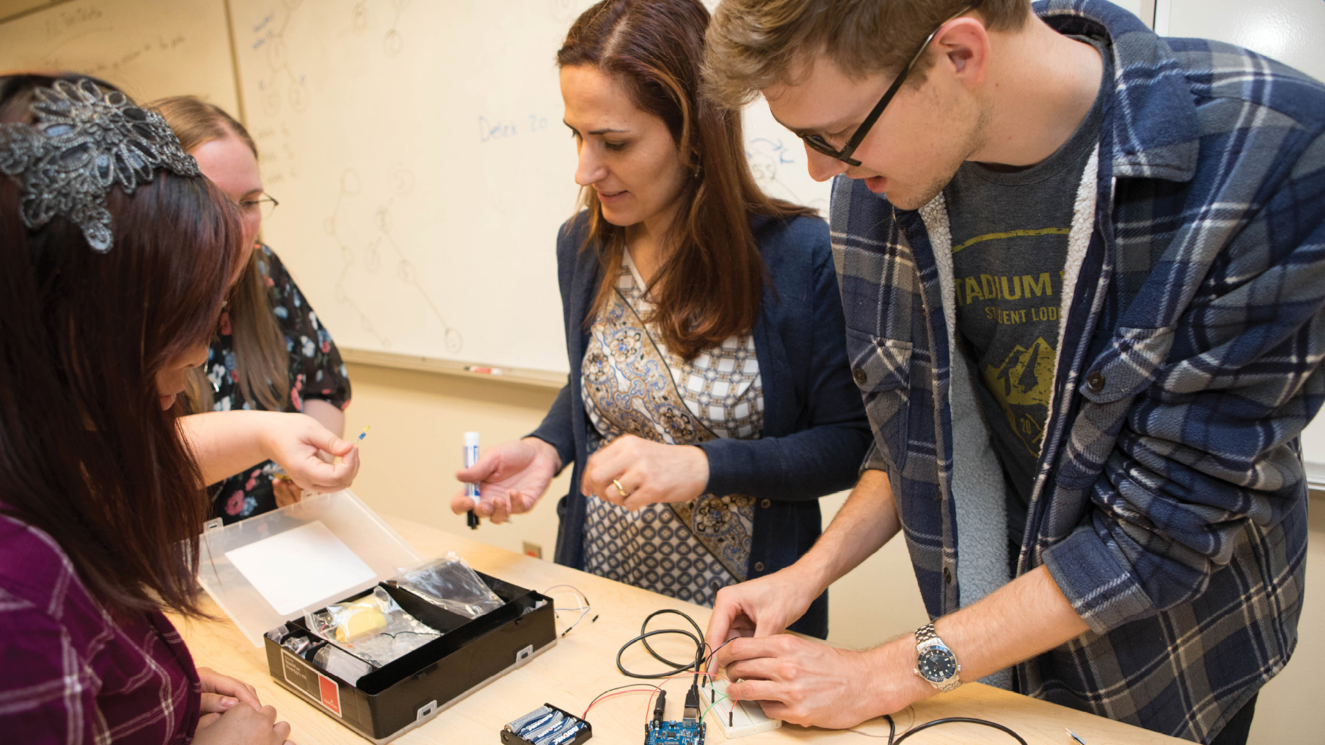 Three students work alongside an instructor to put together a project.