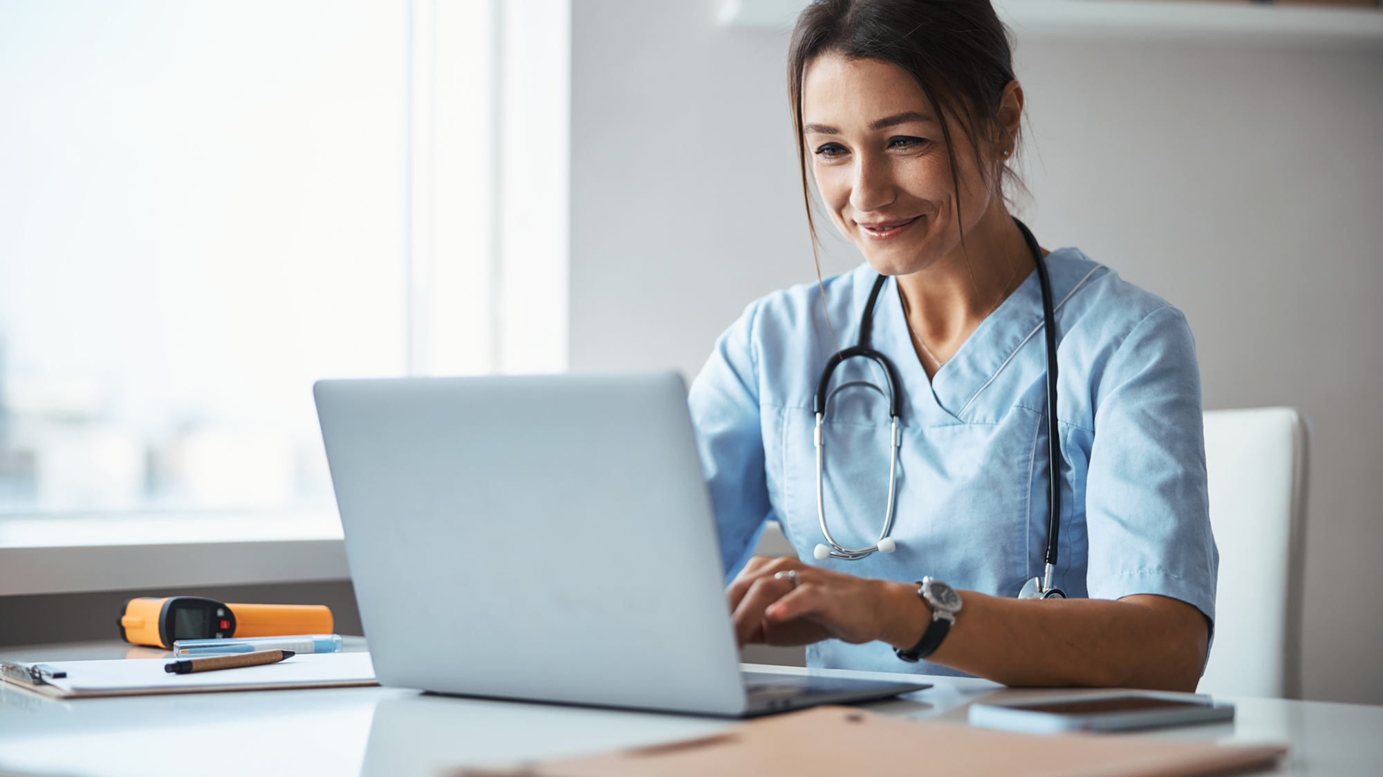 A doctor working on a laptop device at their desk in a clinic.