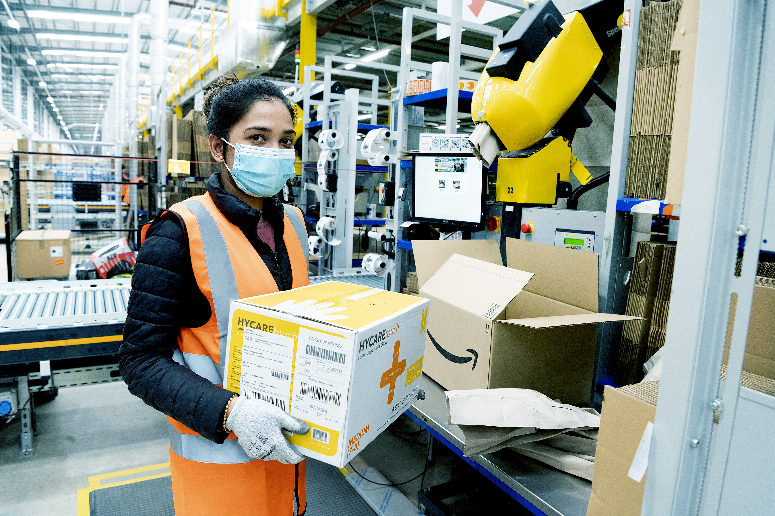 An Amazon fulfilment centre employee packing boxes with medical supplies in the Coalville Fulfilment centre to provide supplies to the relevant government centres. She is wearing protective gloves and a face mask.