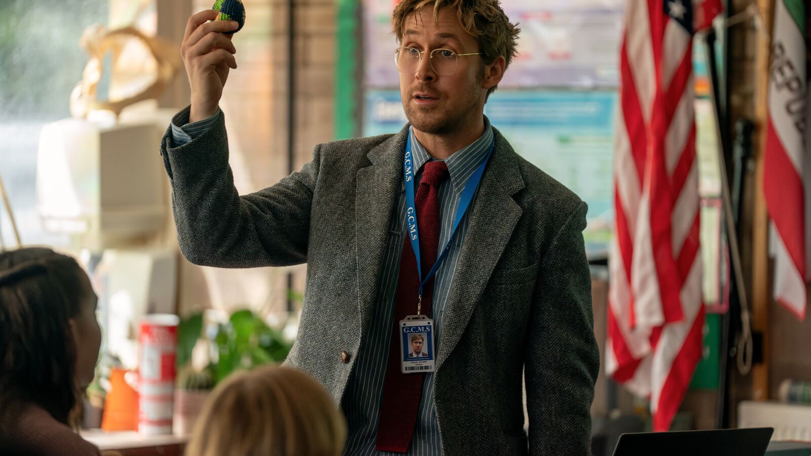 A scene from Project Hail Mary starring Ryan Gosling in a classroom demonstrating object, flag in background