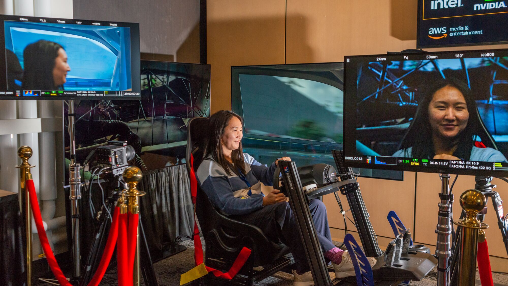 author connie chen sitting in a car shell pretending to drive a car while her face is projected onto screens that show her racing around a racetrack