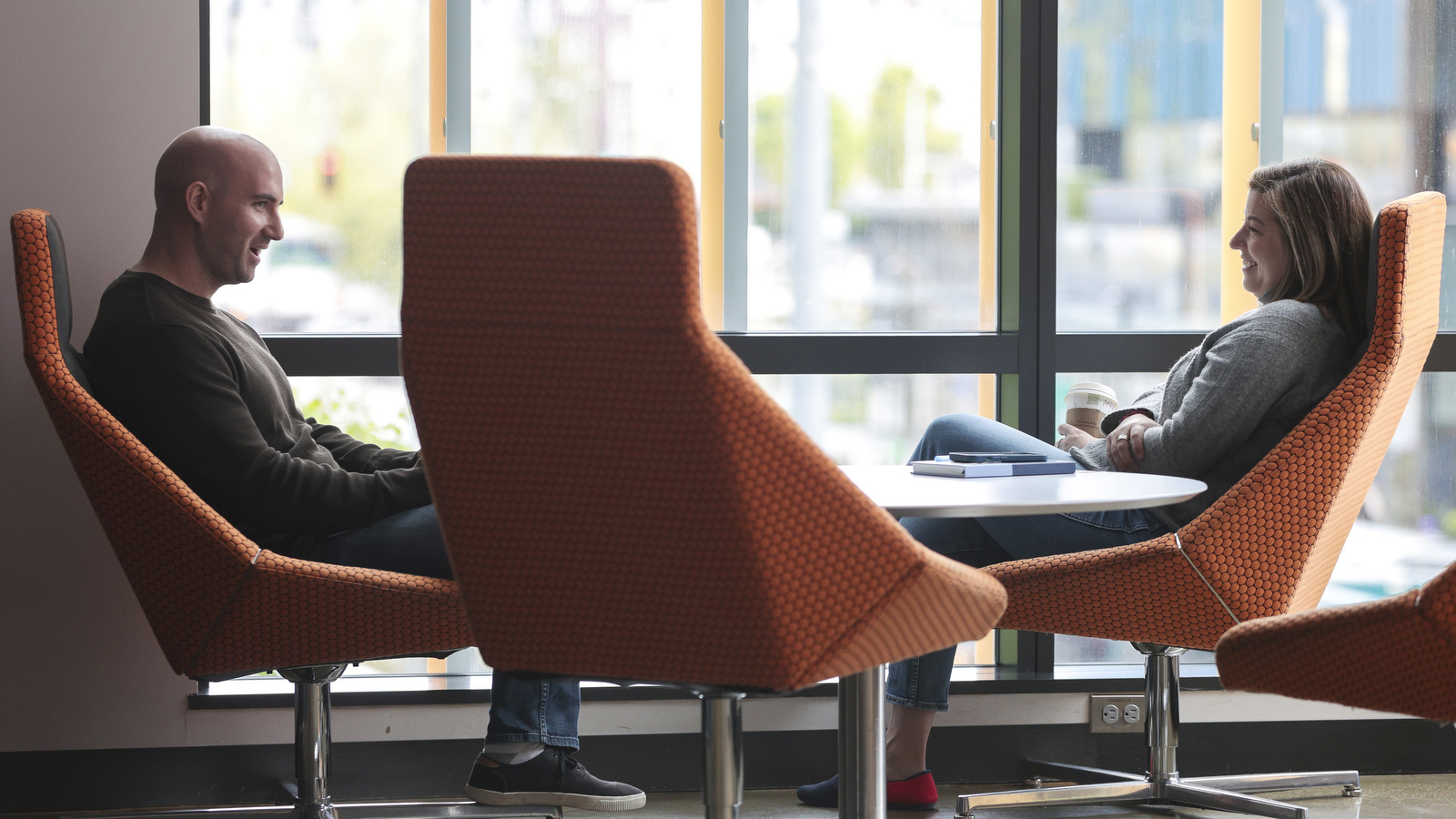 Two Amazon employees sitting in funky orange seats next to a window.