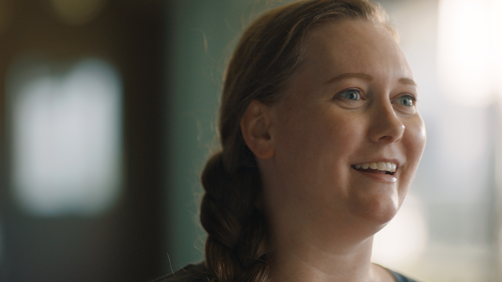 A close-up portrait image of a woman smiling while looking off into the distance.