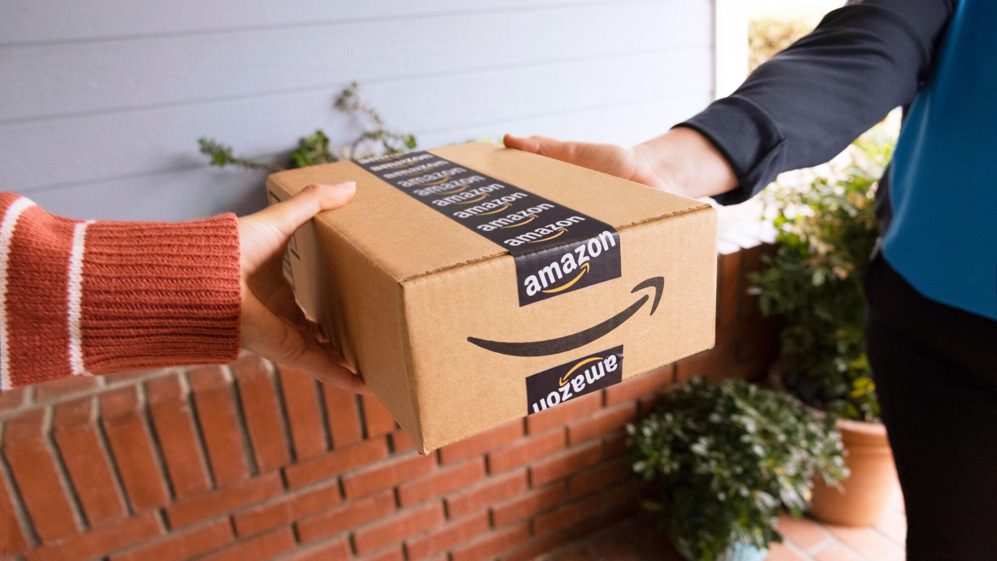 Delivery person passing Amazon box on brick porch with foliage