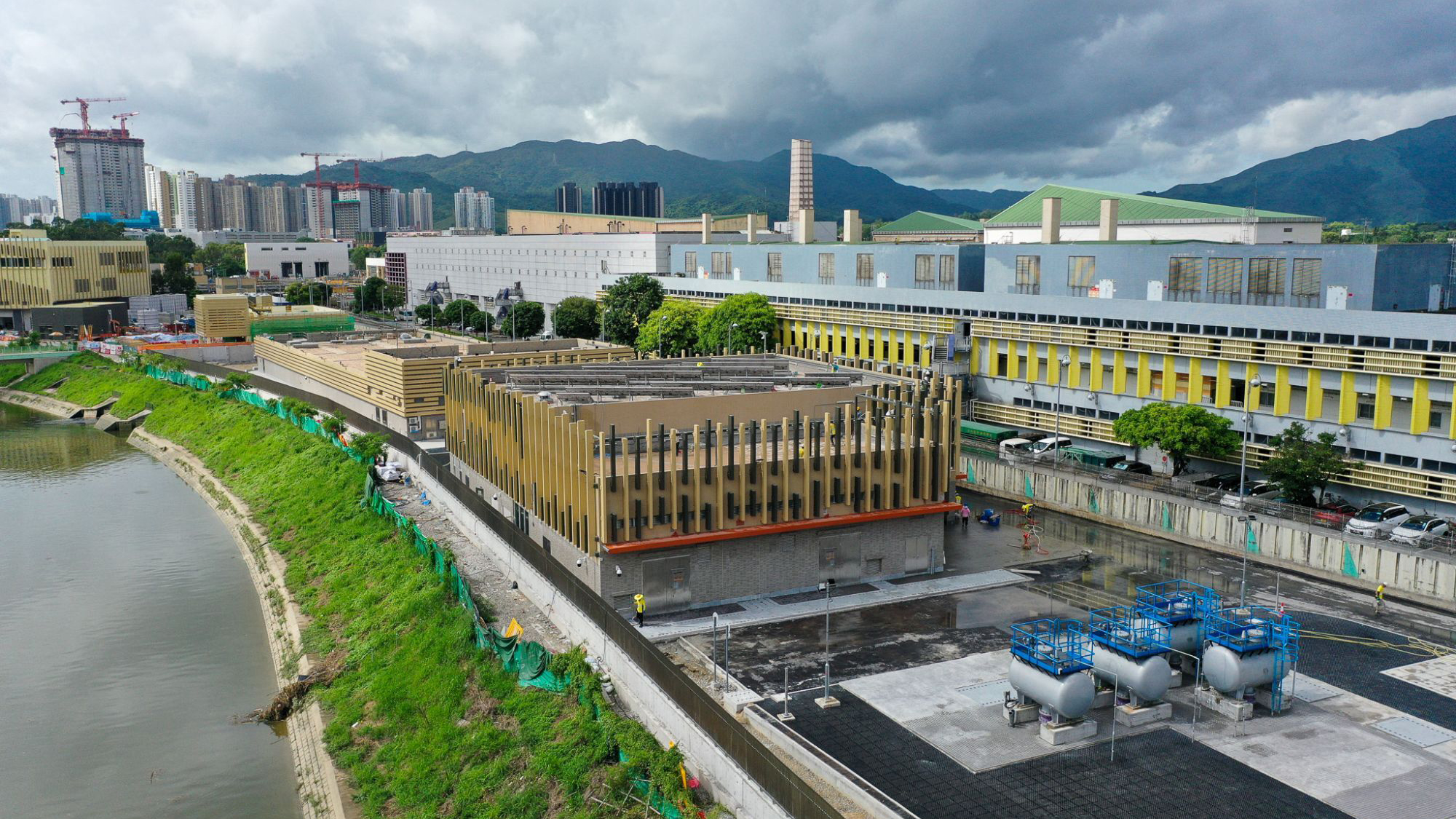 Hong Kong: Urban development along riverbank with industrial facility and mountains in background