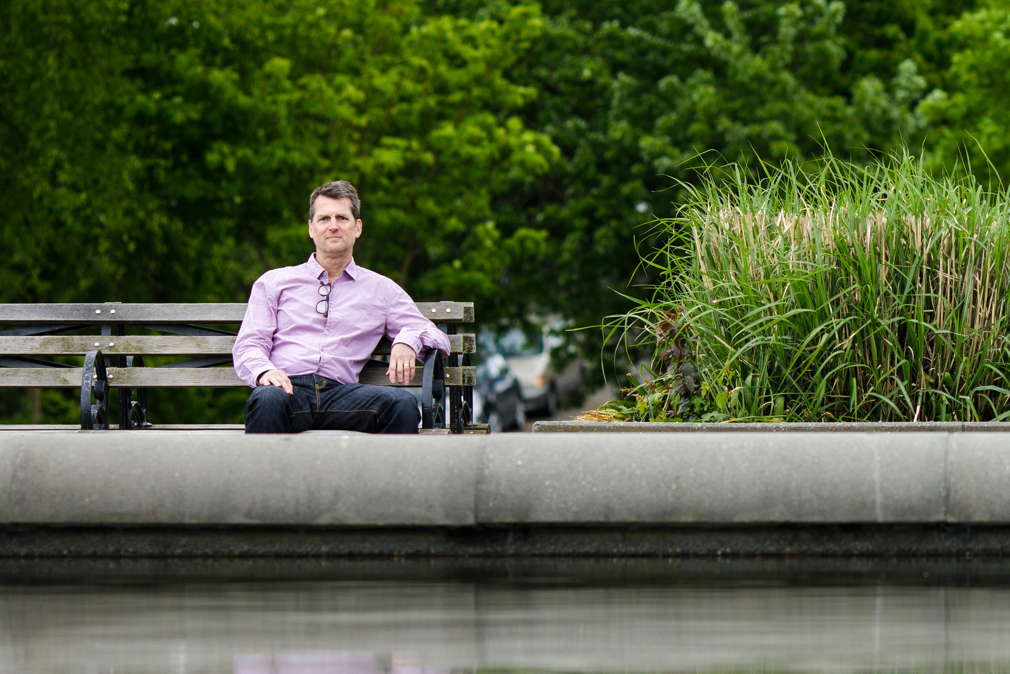 Amazon employee Neal Thompson sits on a bench. He wears a purple button-down shirt. A pair of glasses hang from his open color.