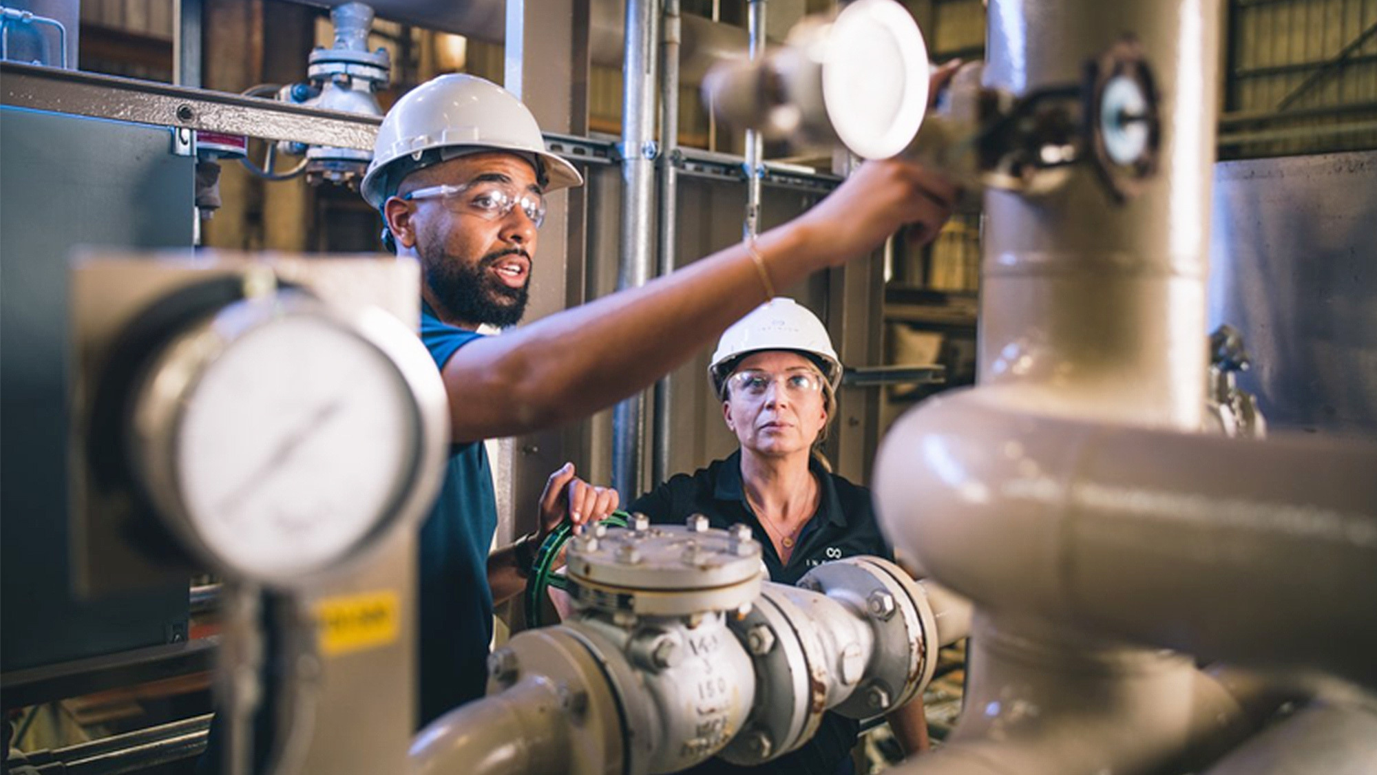 An image of a man and a woman wearing white helmets and clear glasses at a lab. 