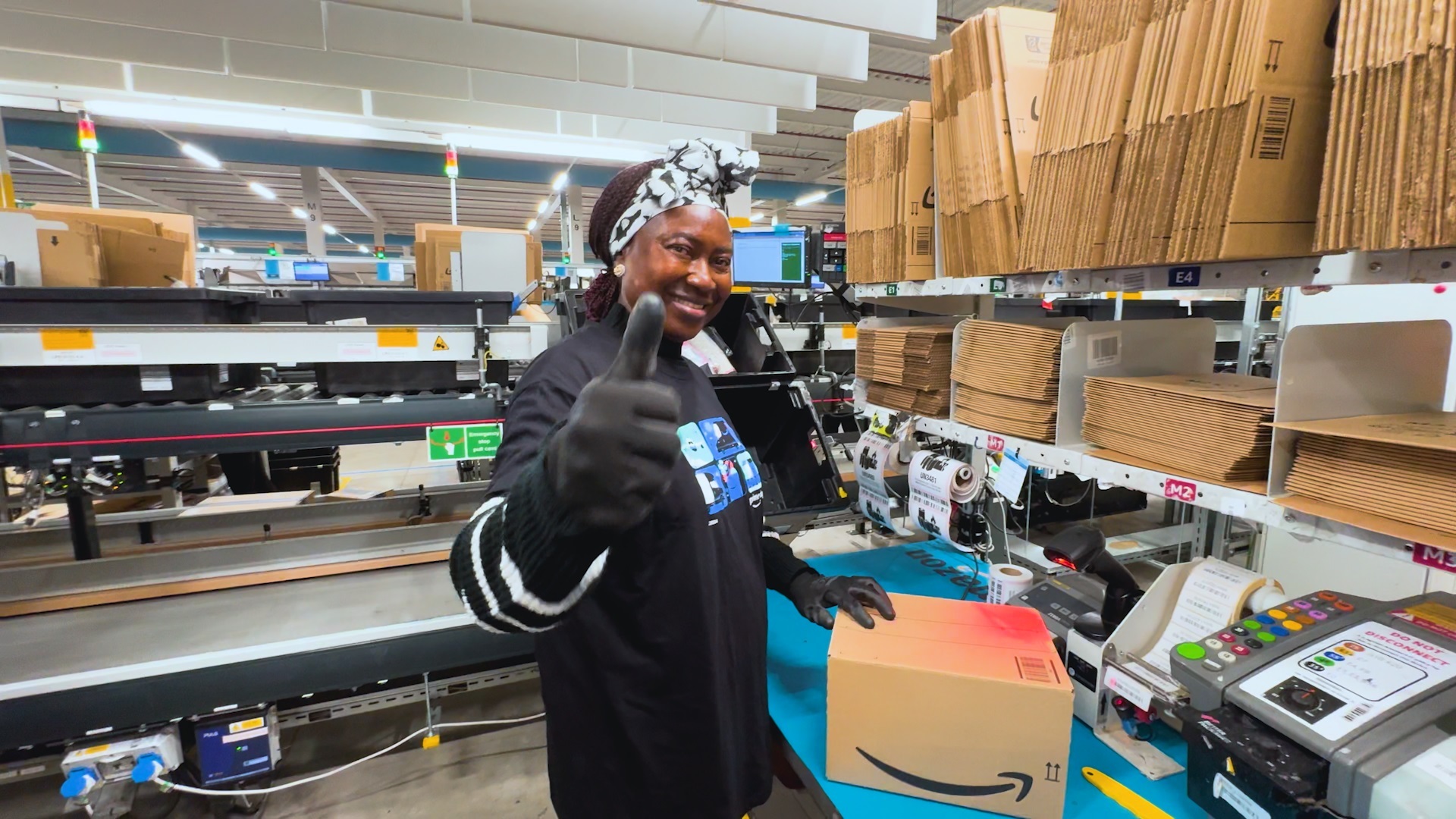 An Amazon fulfilment centre employee showing a thumbs-up while preparing a package for delivery.