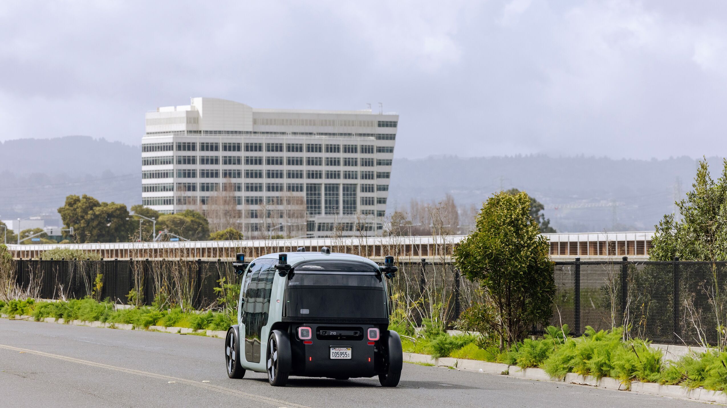 an image of a Zoox robotaxi driving down a road with a building in the background.