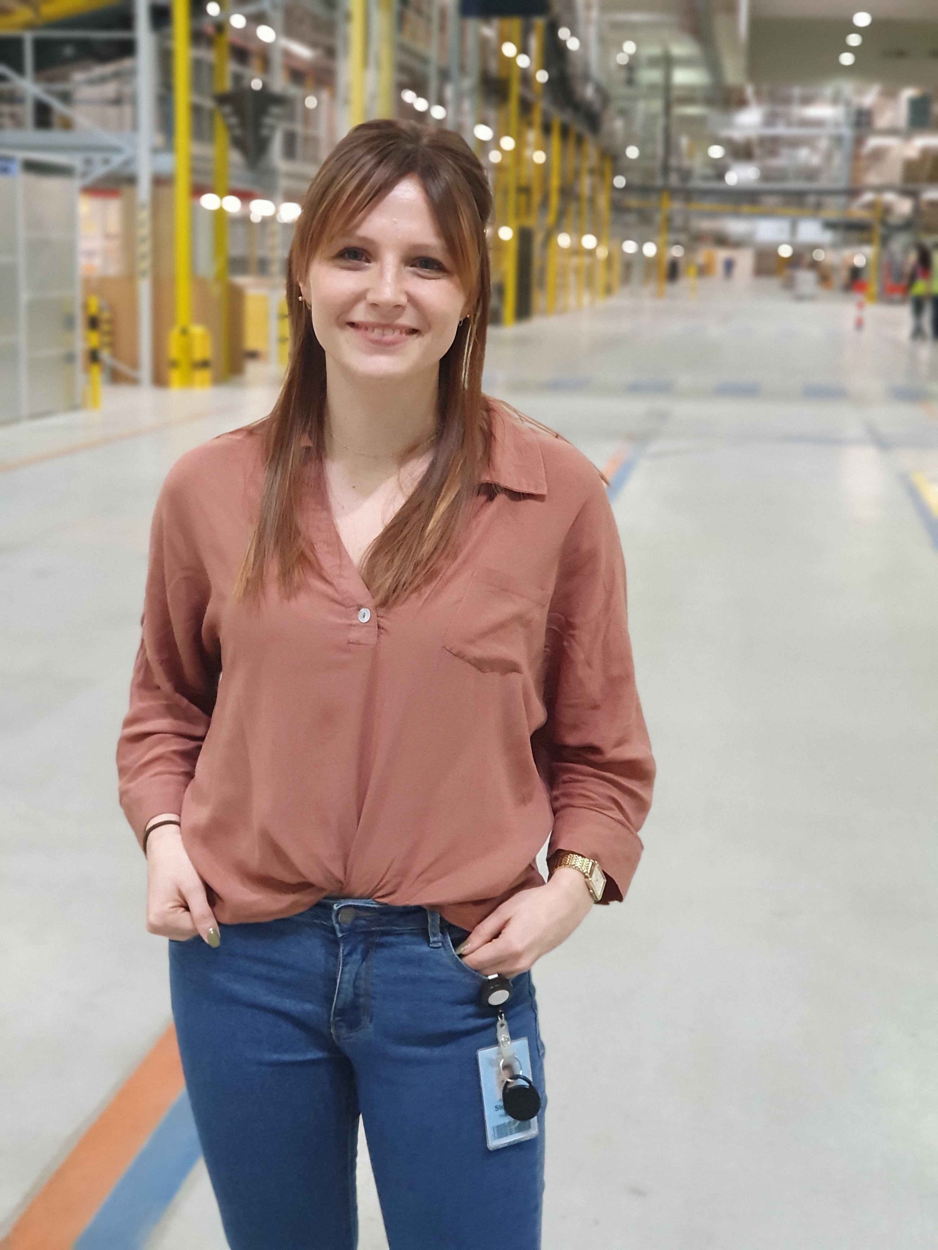 Eine junge Frau in Bluse und Jeans steht in einer Logistikhalle