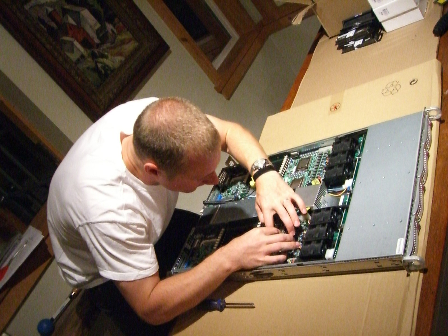 An image of a man working on the motherboard of a computer in a low-lit room. 