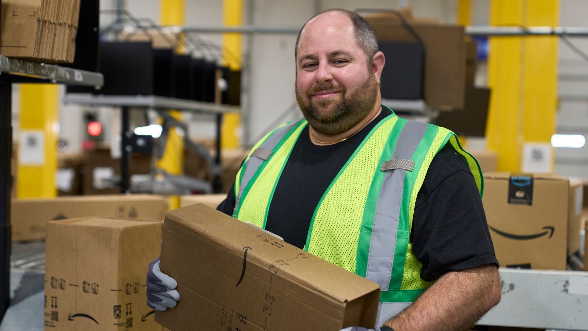 A photo of an Amazon fulfillment center employee holding an Amazon delivery box inside a fulfillment center.