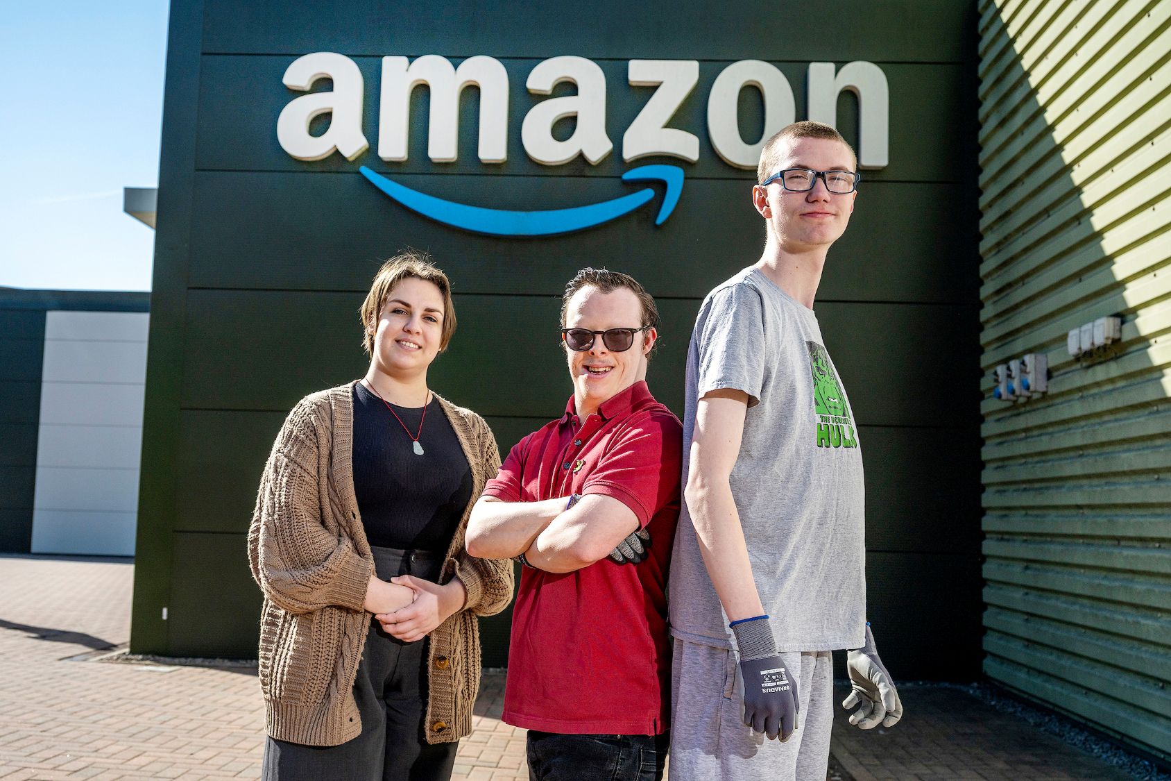 A woman and two men stand outside an Amazon fulfilment centre