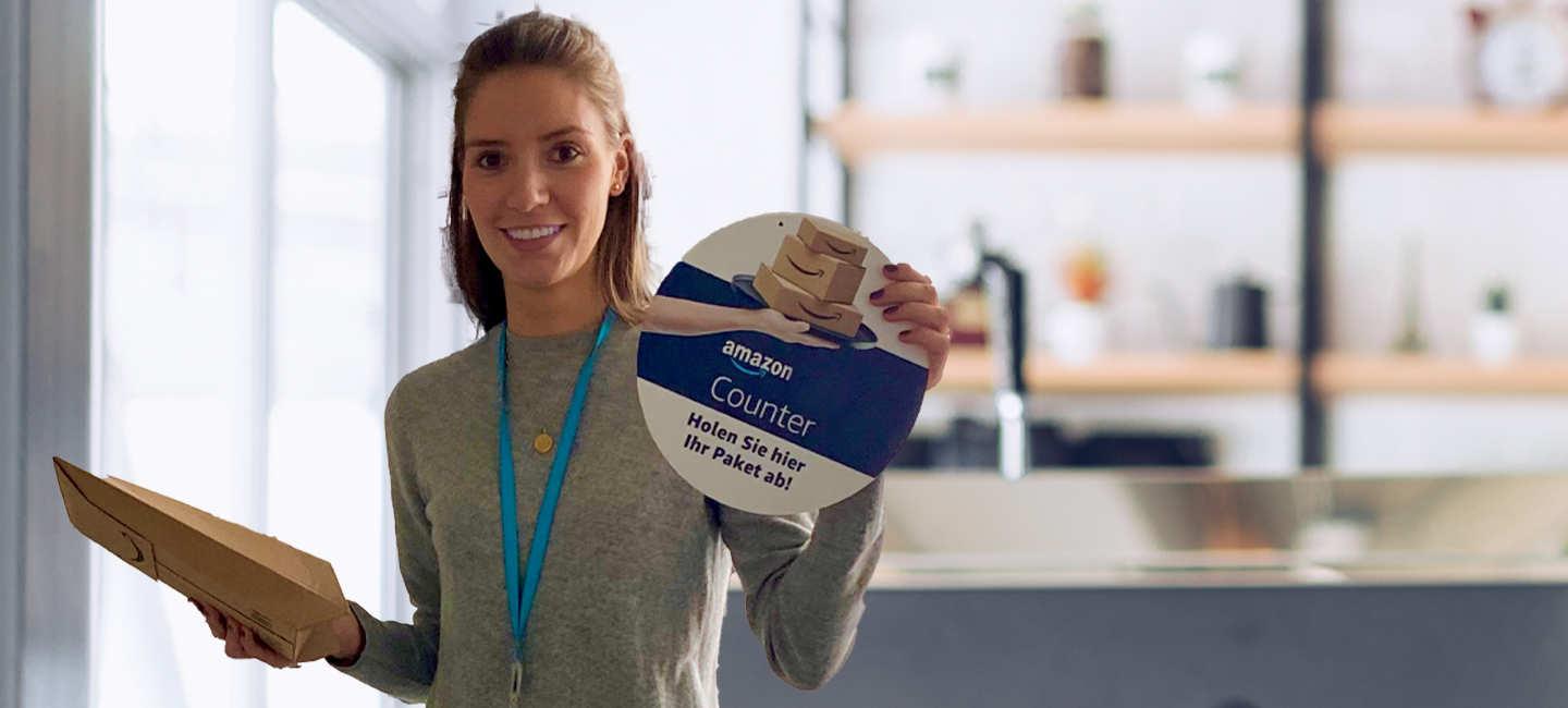Eine junge Frau mit Päckchen und Amazon Counter Schild