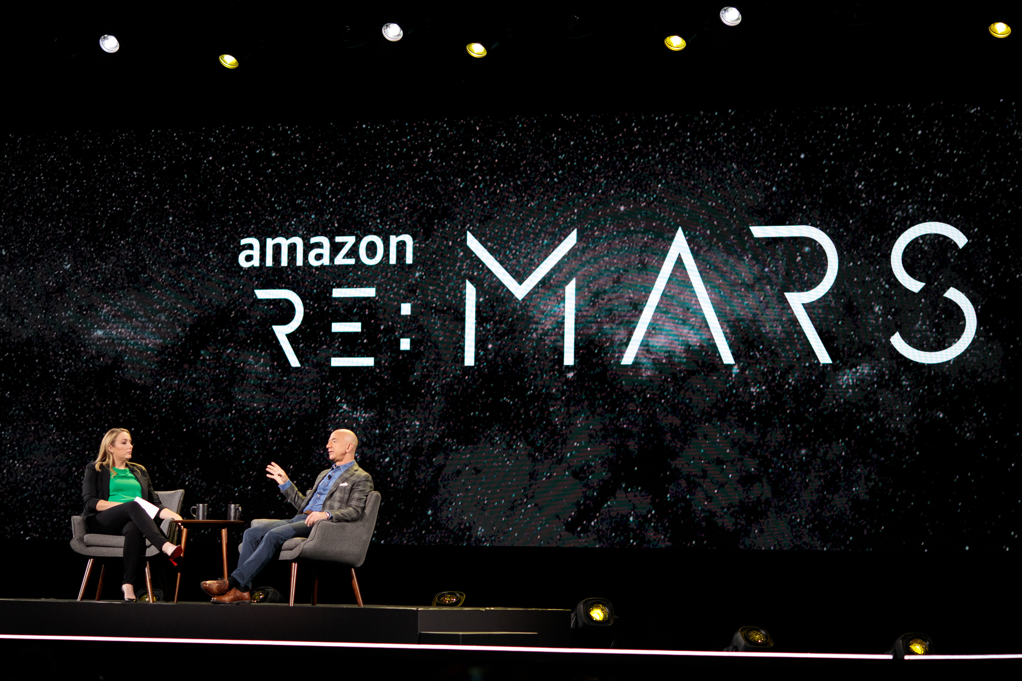 Jeff Bezos and Jenny Freshwater sit in chairs on stage at re:MARS 2019, for a fireside chat.