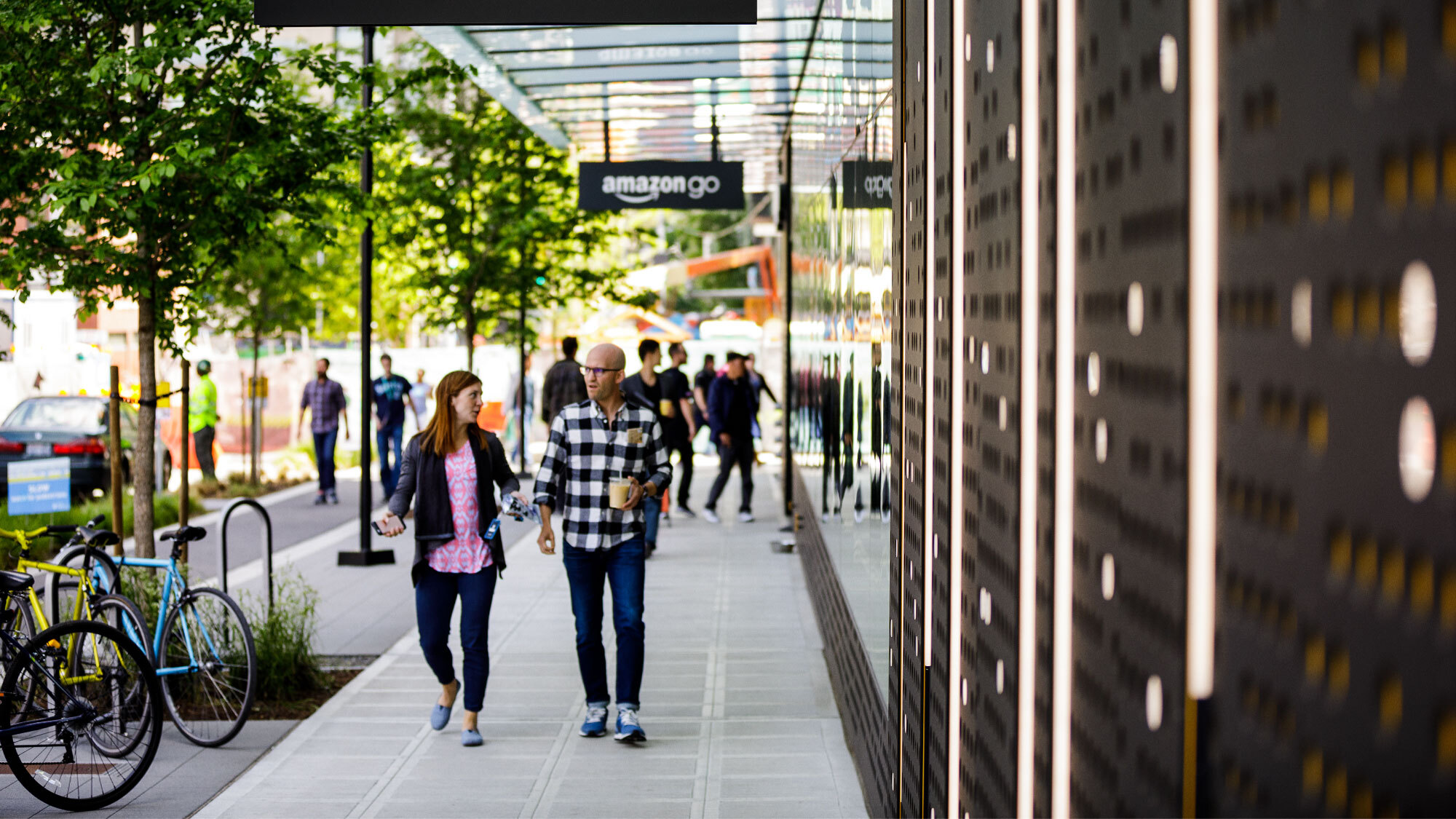 An image of the outside of the Amazon Go store at Amazon's headquarters in Seattle. There are people walking and talking on the sidewalk out front of the store. 