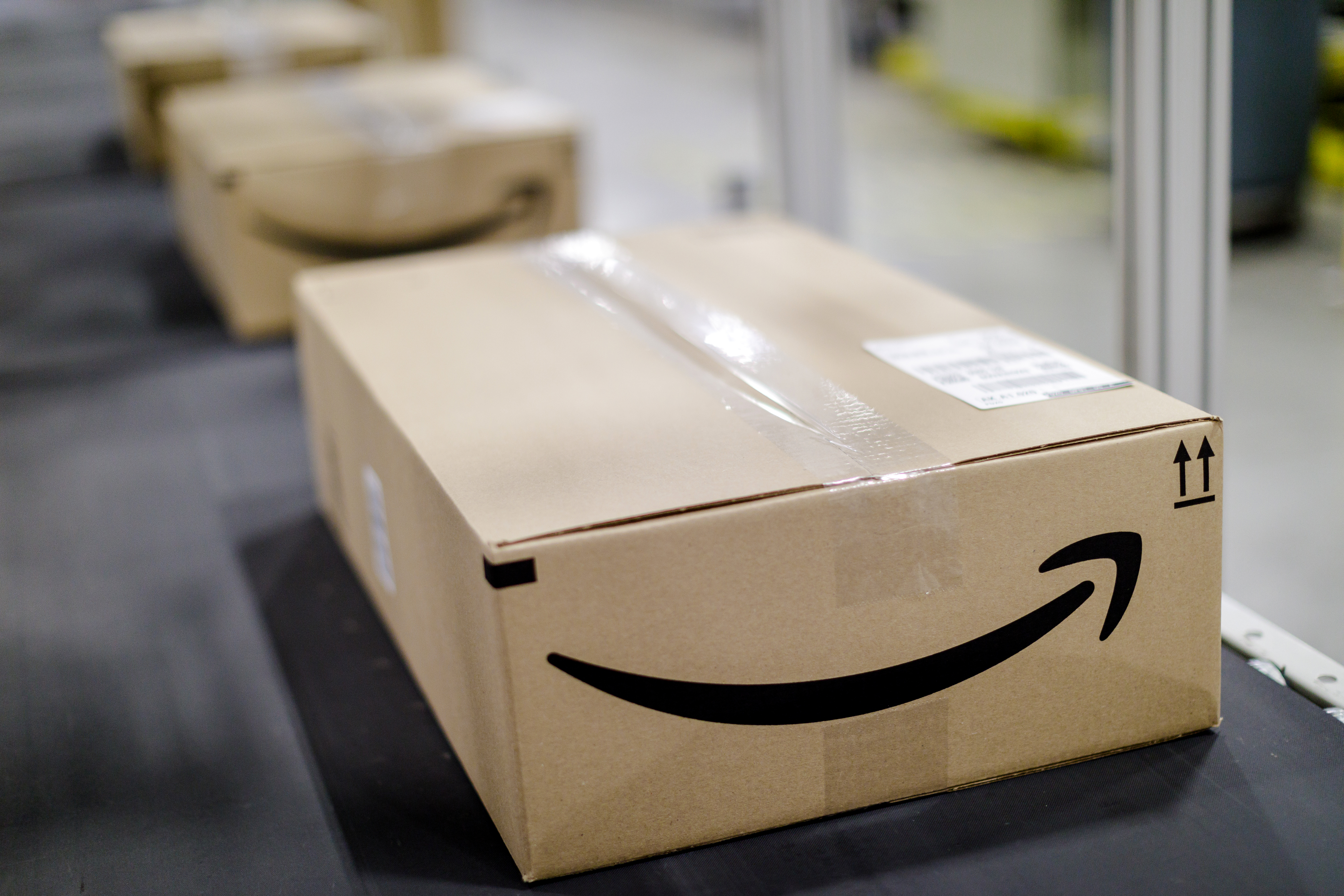 A brown Amazon box on a conveyor belt in an Amazon warehouse. The Amazon smile logo is on the side. 