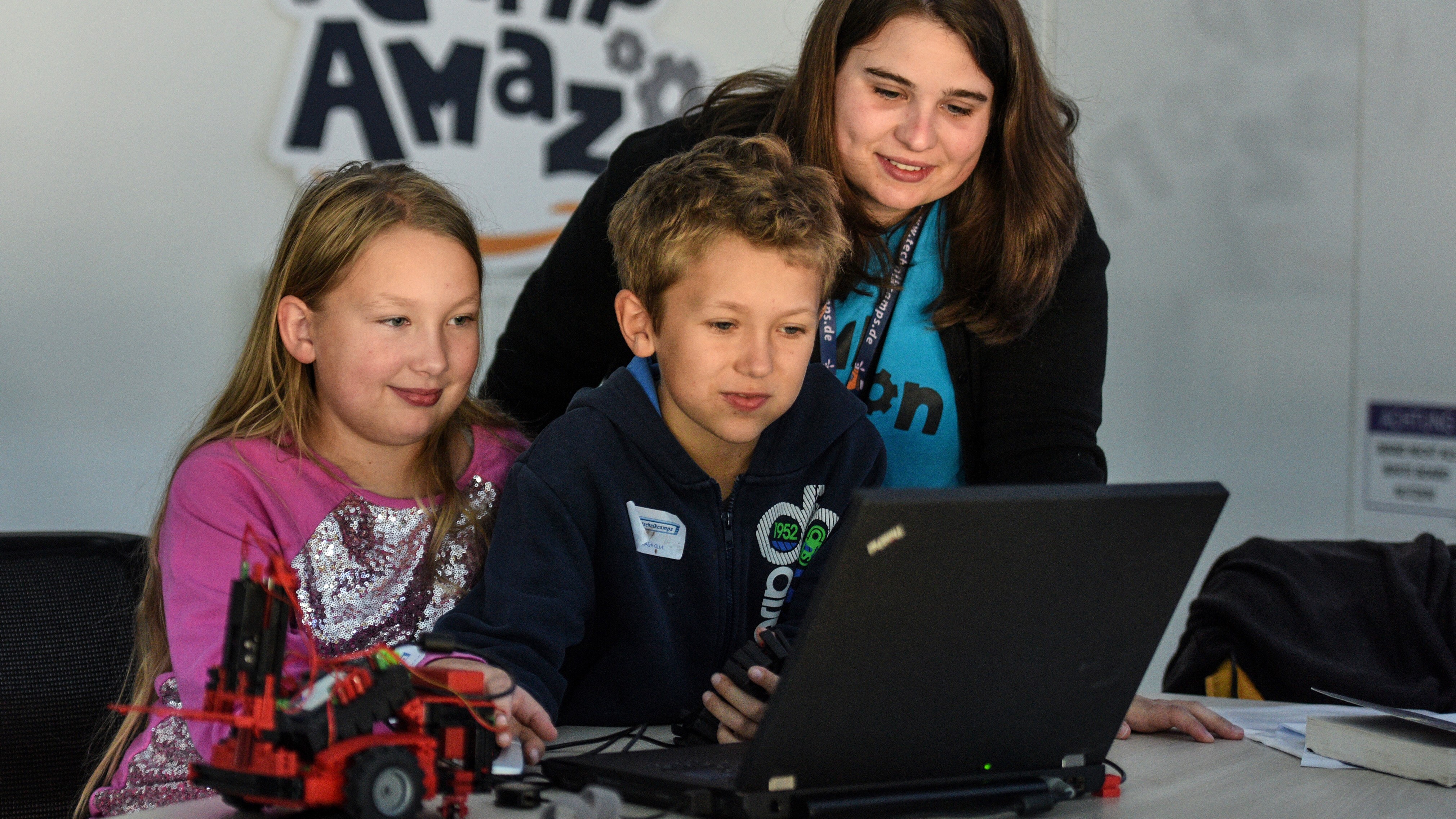 2 Kinder am PC, im Hintergrund sieht man eine Betreuerin, die ebenfalls in den Laptop blickt.