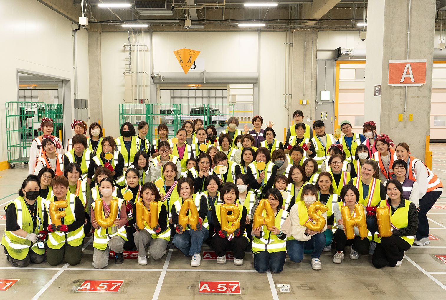 たくさんの女性たちが倉庫のような場所で集まってポーズしている。前にいる女性たちは「Funabashi」の風船を持っている。