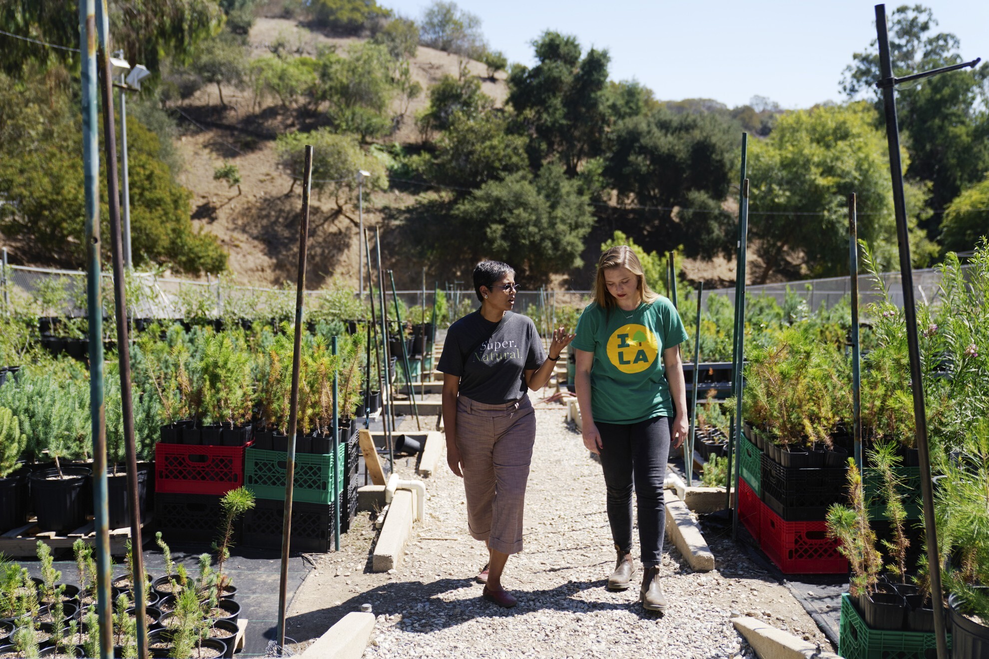 Two woman walk and talk through a community garden.