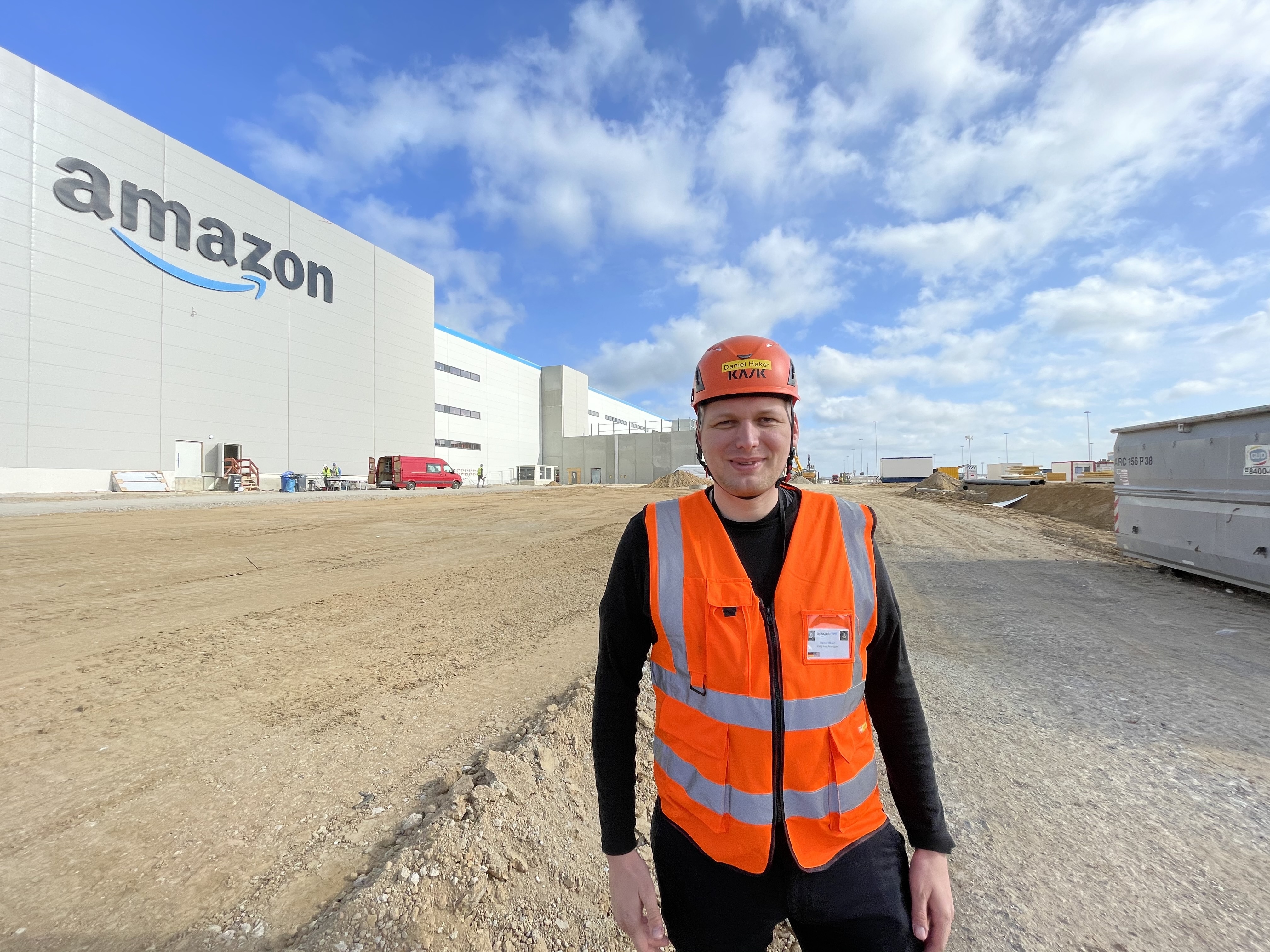 Daniel mit Helm und Sicherheitsweste vor dem neuen Logistikzentrum in Gera.