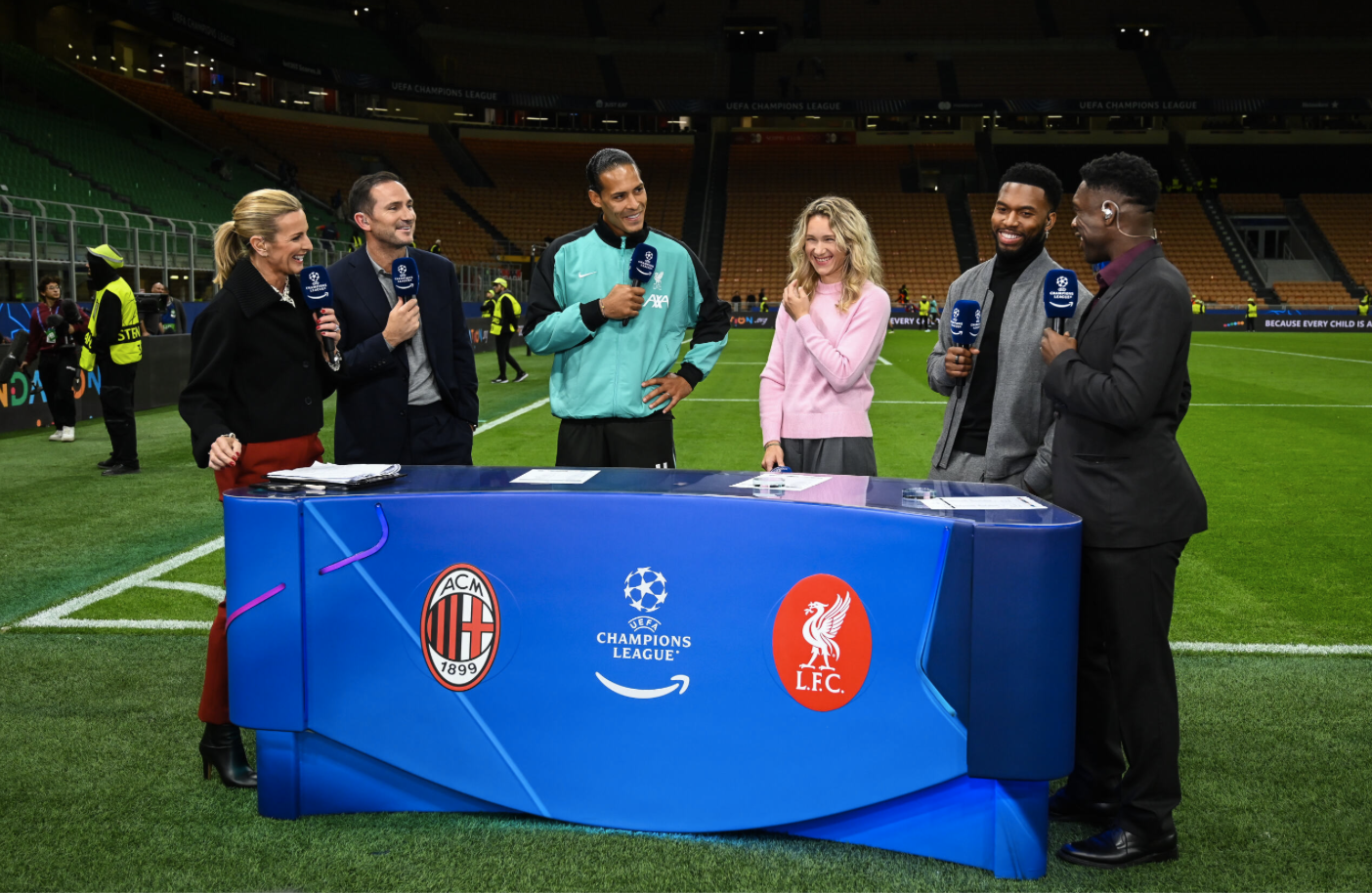 A still from Prime Video's coverage of the Champions League, showing pundits behind a pitch-side desk with microphones