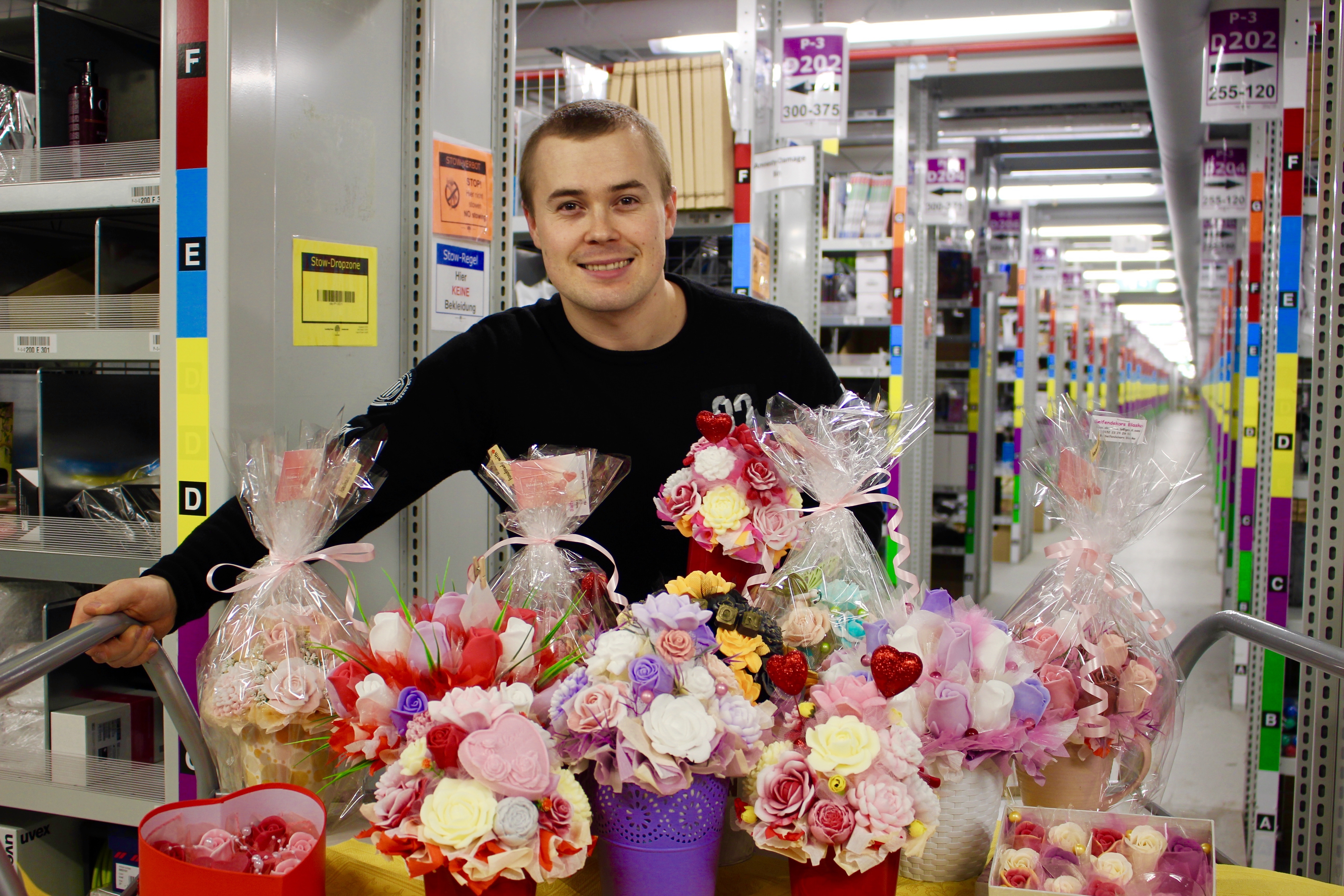 Juraj steht im Logistikzentrum, vor ihm eine bunte Palette an Seifensträußen
