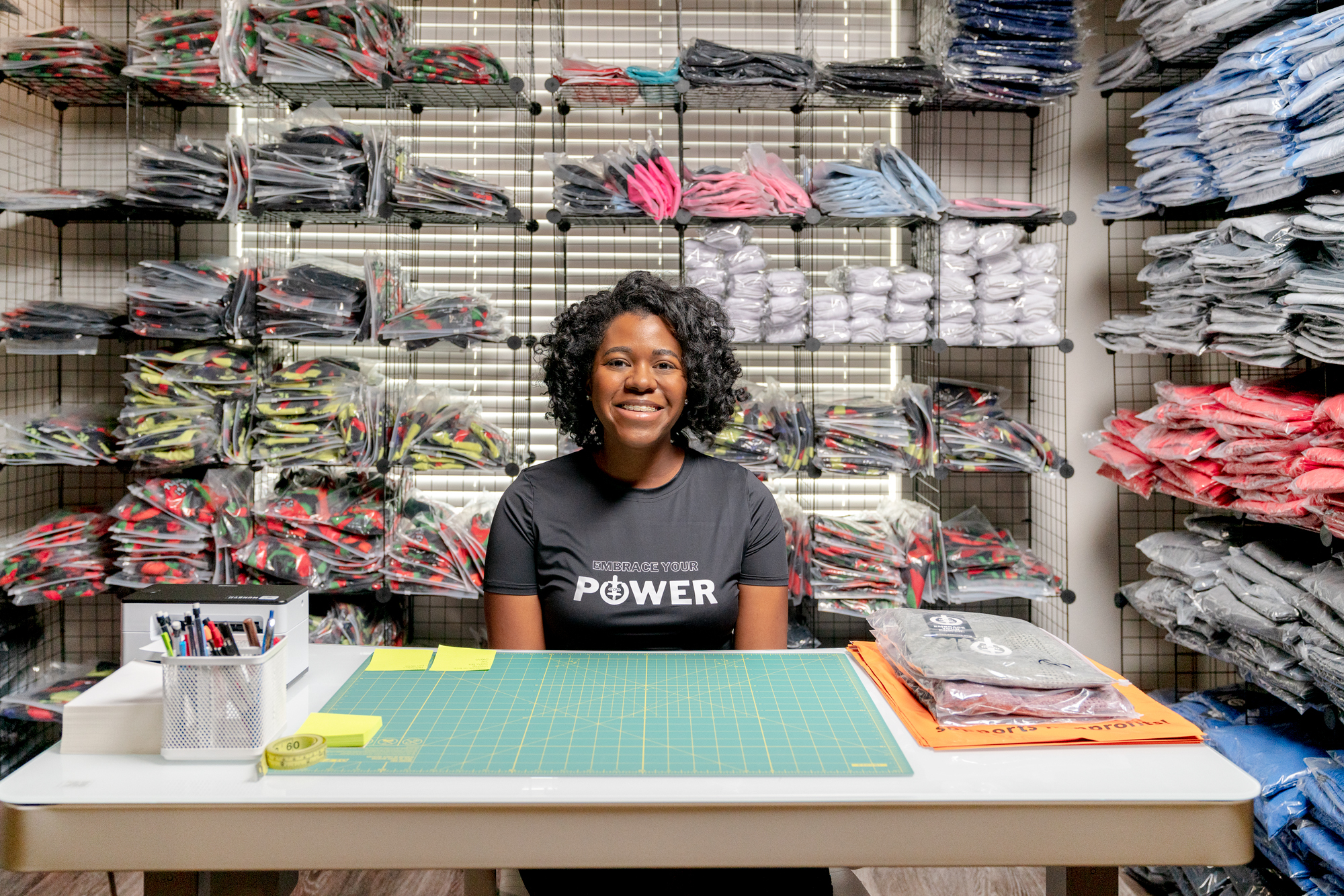 Angel Johnson sits at her desk and smiles surrounded by packaged ICONI apparel.