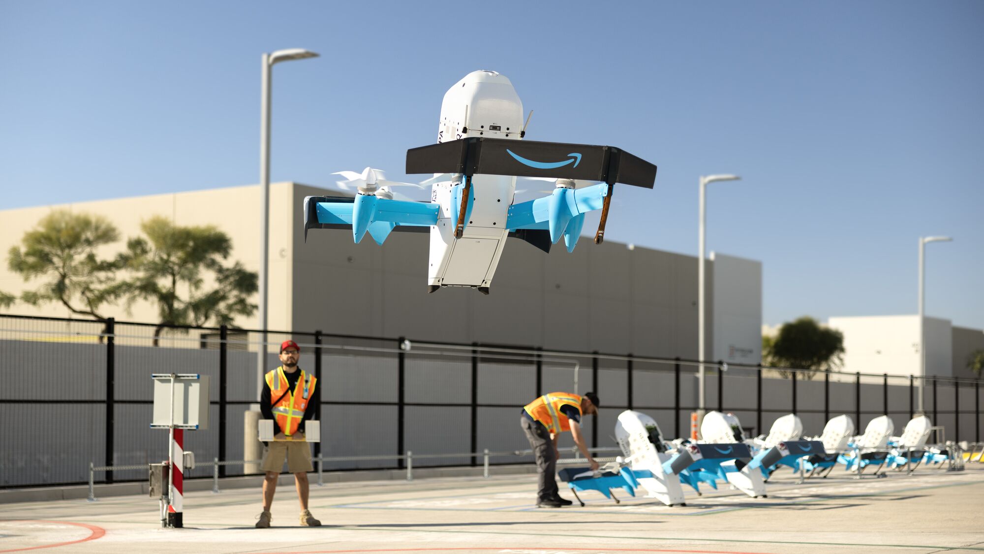 Amazon Prime Air drone demonstration in outdoor testing facility with employees in safety vests