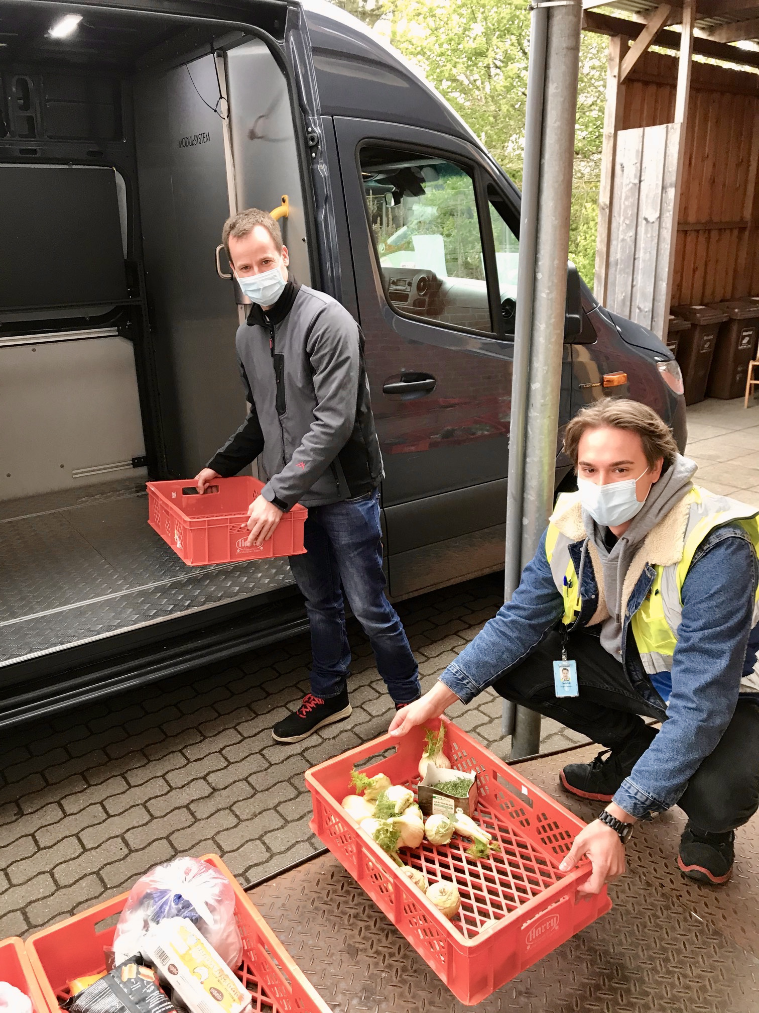 Ein Amazon Mitarbeiter belädt gemeinsam mit einem Tafel-Helfer das Lieferfahrzeug. Beide tragen Masken.