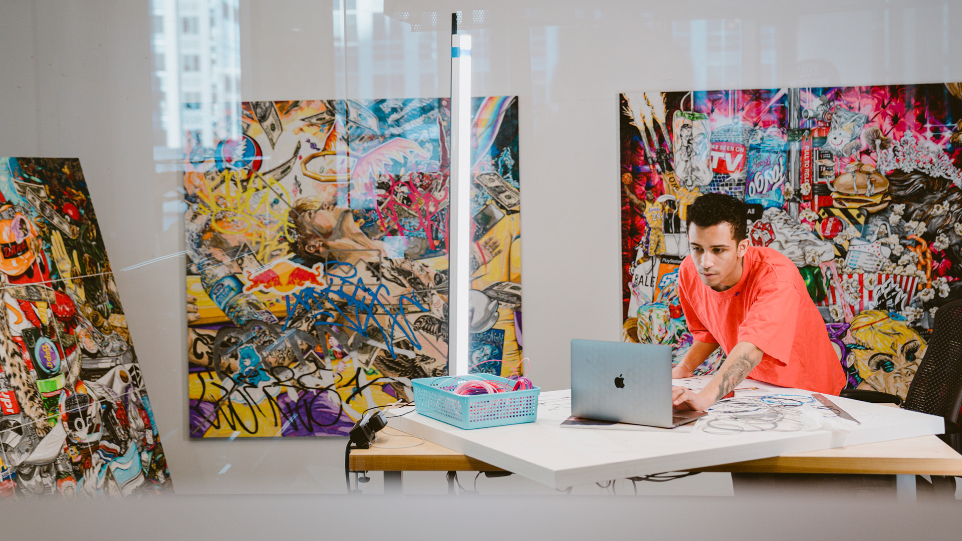 An artist in residence showcase his art behind him while he works on his laptop.