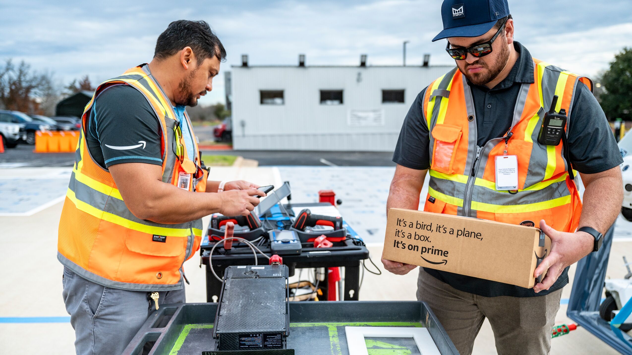 Two employees prepare a package to be loaded onto a drone while standing on the launch pad