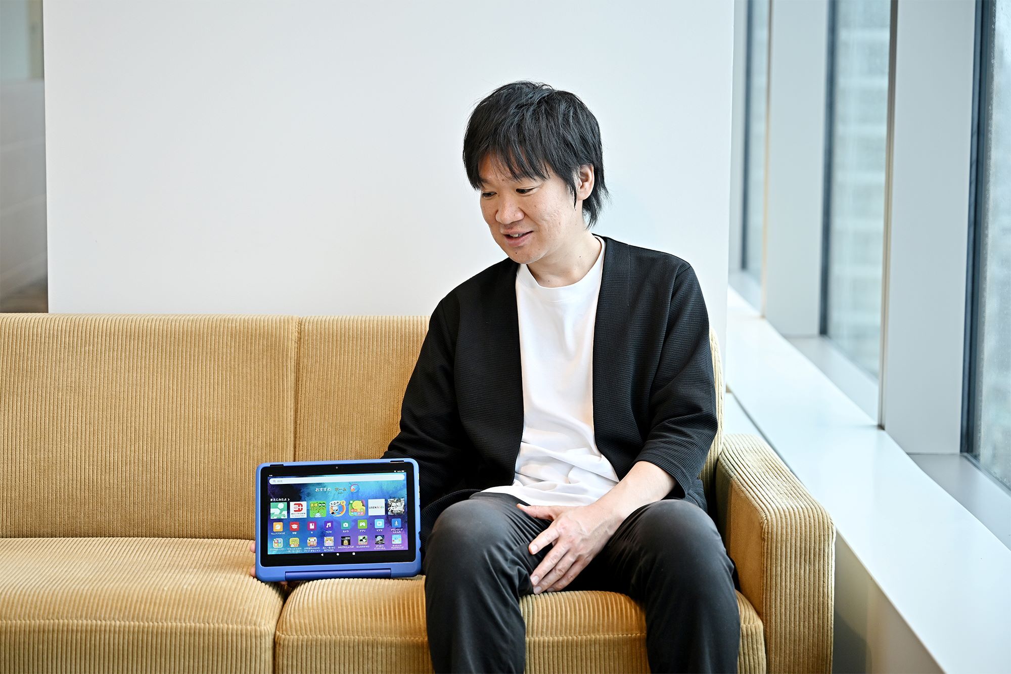 座っている男性がソファに置かれているタブレットを見ている。