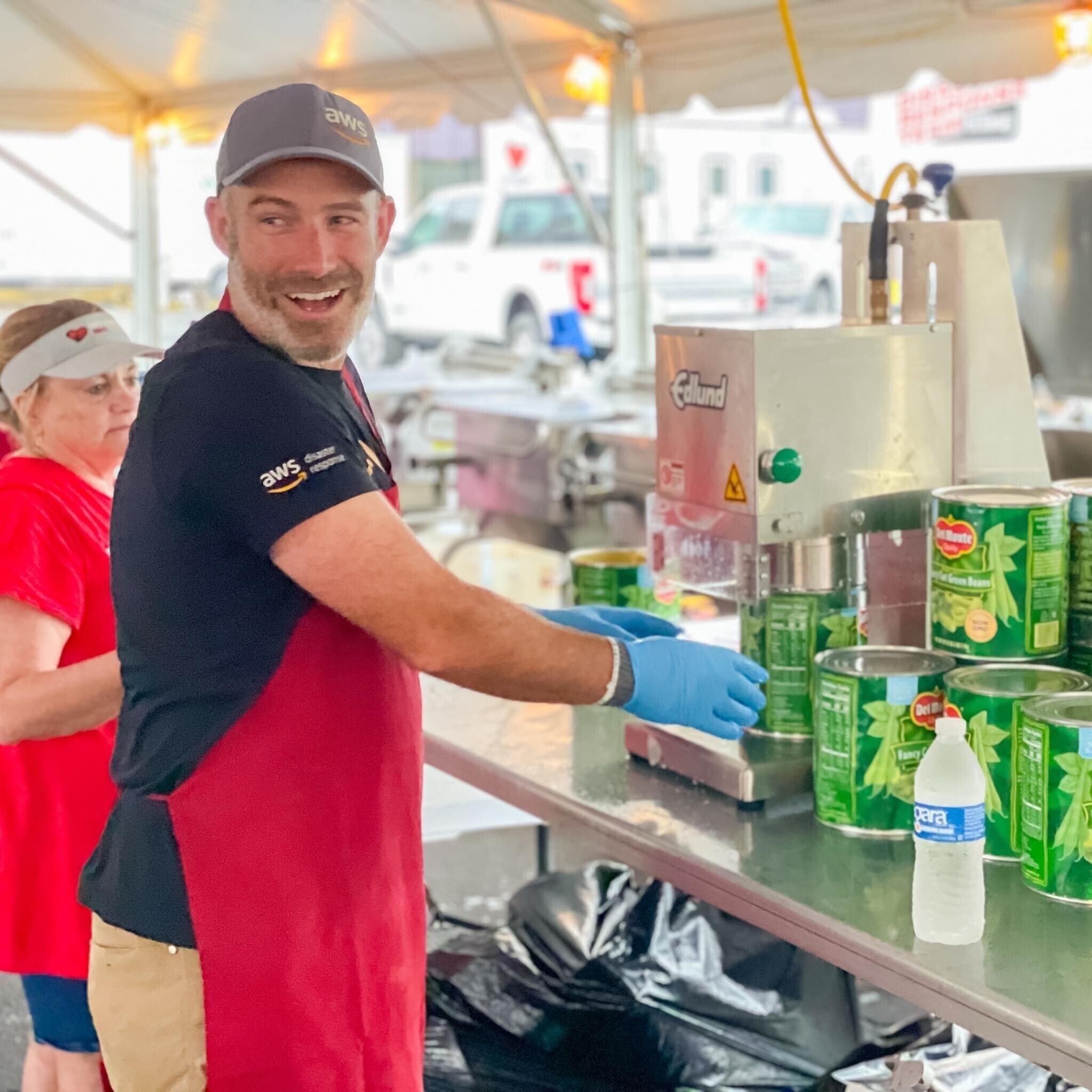 Matt Idalia wears a red apron and opens up cans of green beans as he volunteers for AWS Disaster Response.