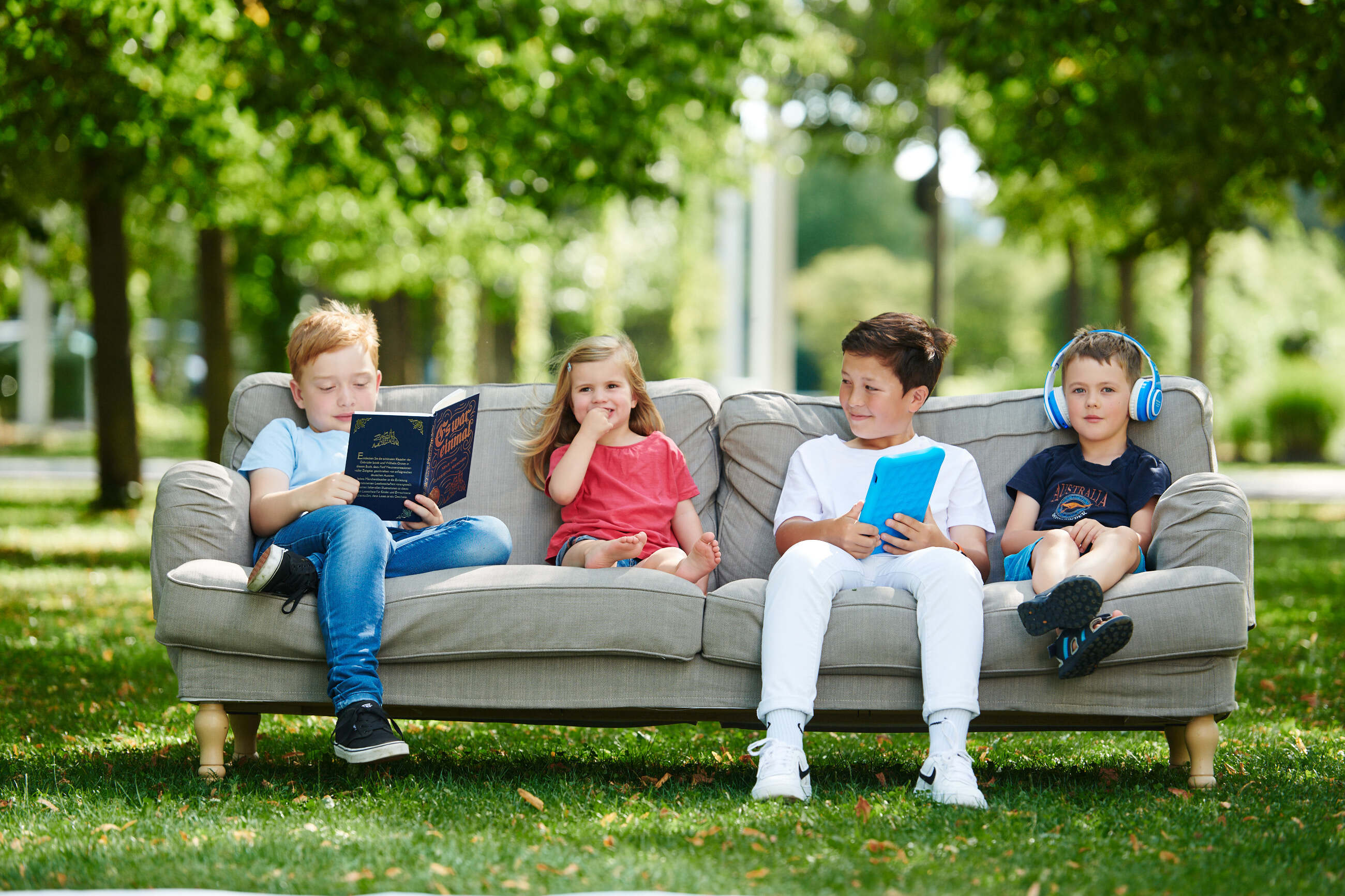 Kinder sitzen im Freien auf einer Couch und lesen Märchen