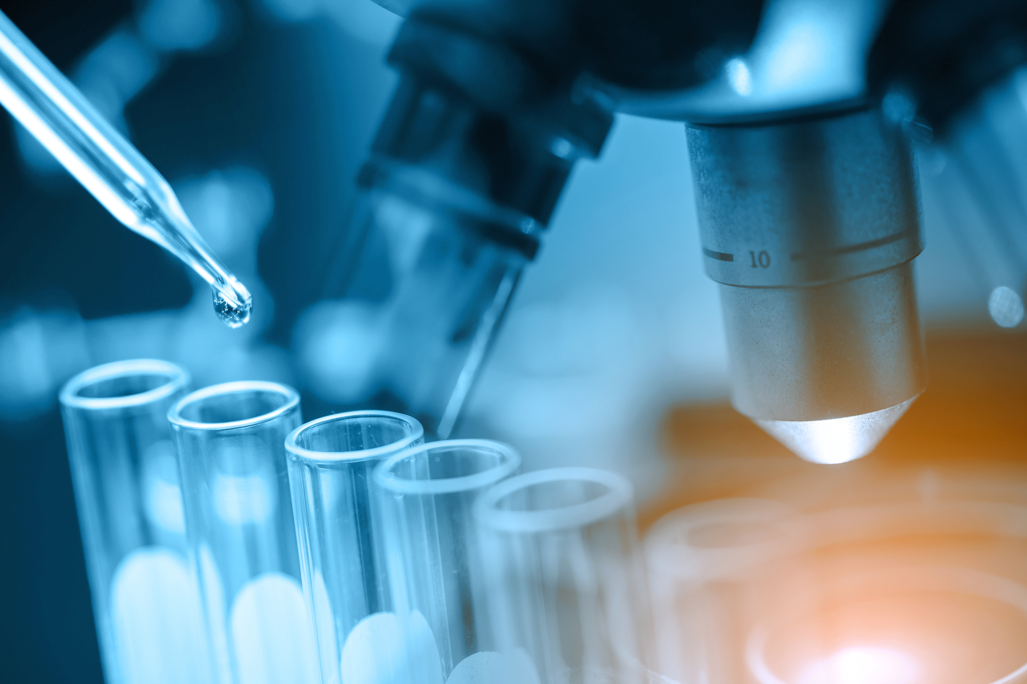 A microscope, test tubes, and a pipette with a drop of liquid emerging.