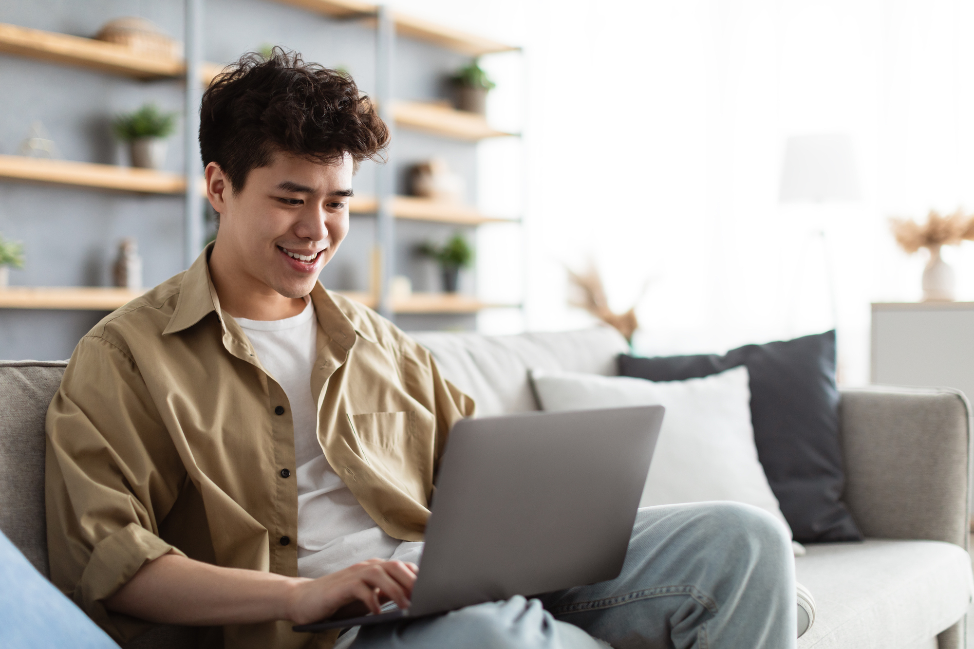 Portrait Of Smiling Man Sitting On The Couch Working On Pc Laptop Indoors In Living Room