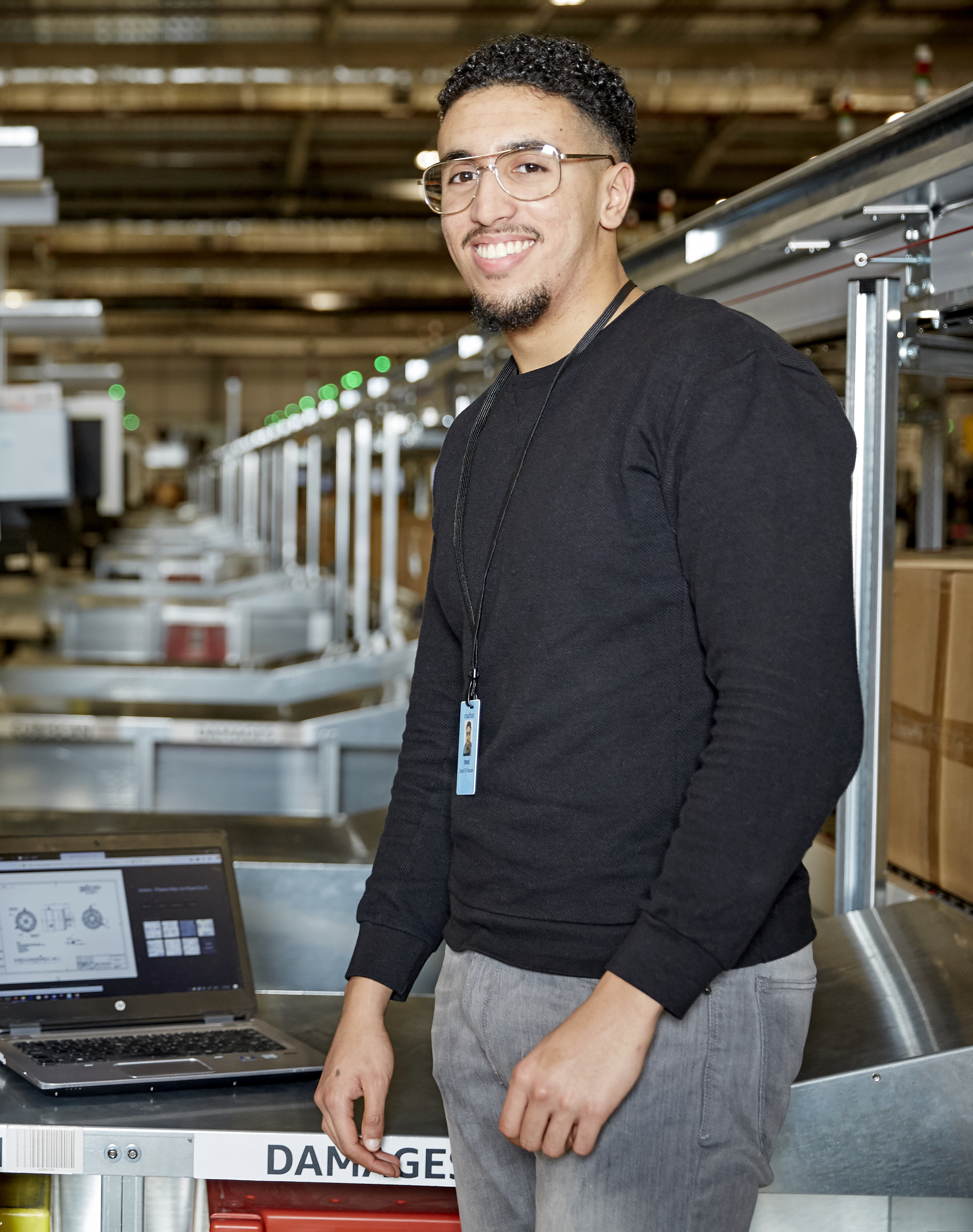 A close up photo of Imad smiling at the camera inside an Amazon warehouse