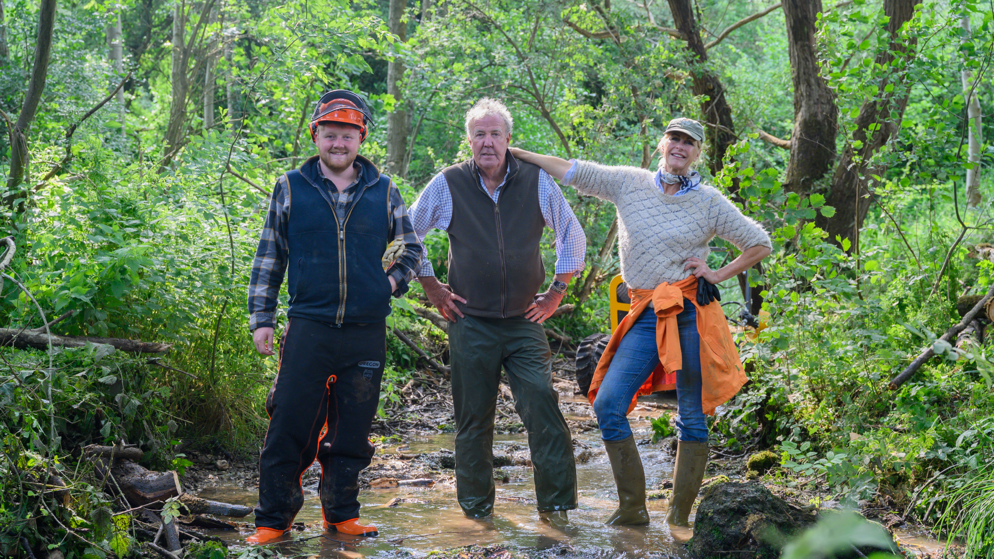Three people standing in a forest stream wearing work gear and safety equipment