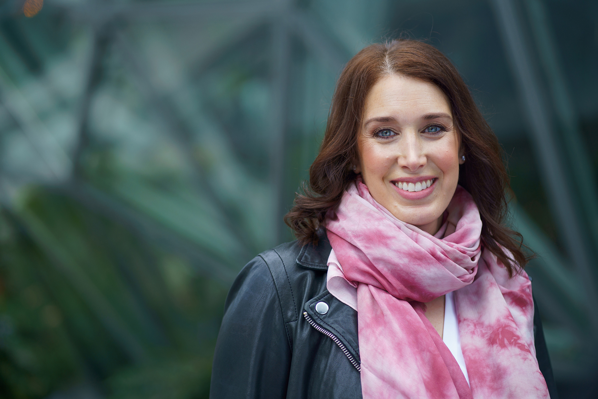 Sarah Gelman smiles for a photo in front of the Spheres at Amazon's headquarters in Seattle. She is wearing a pink scarf and a leather jacket.