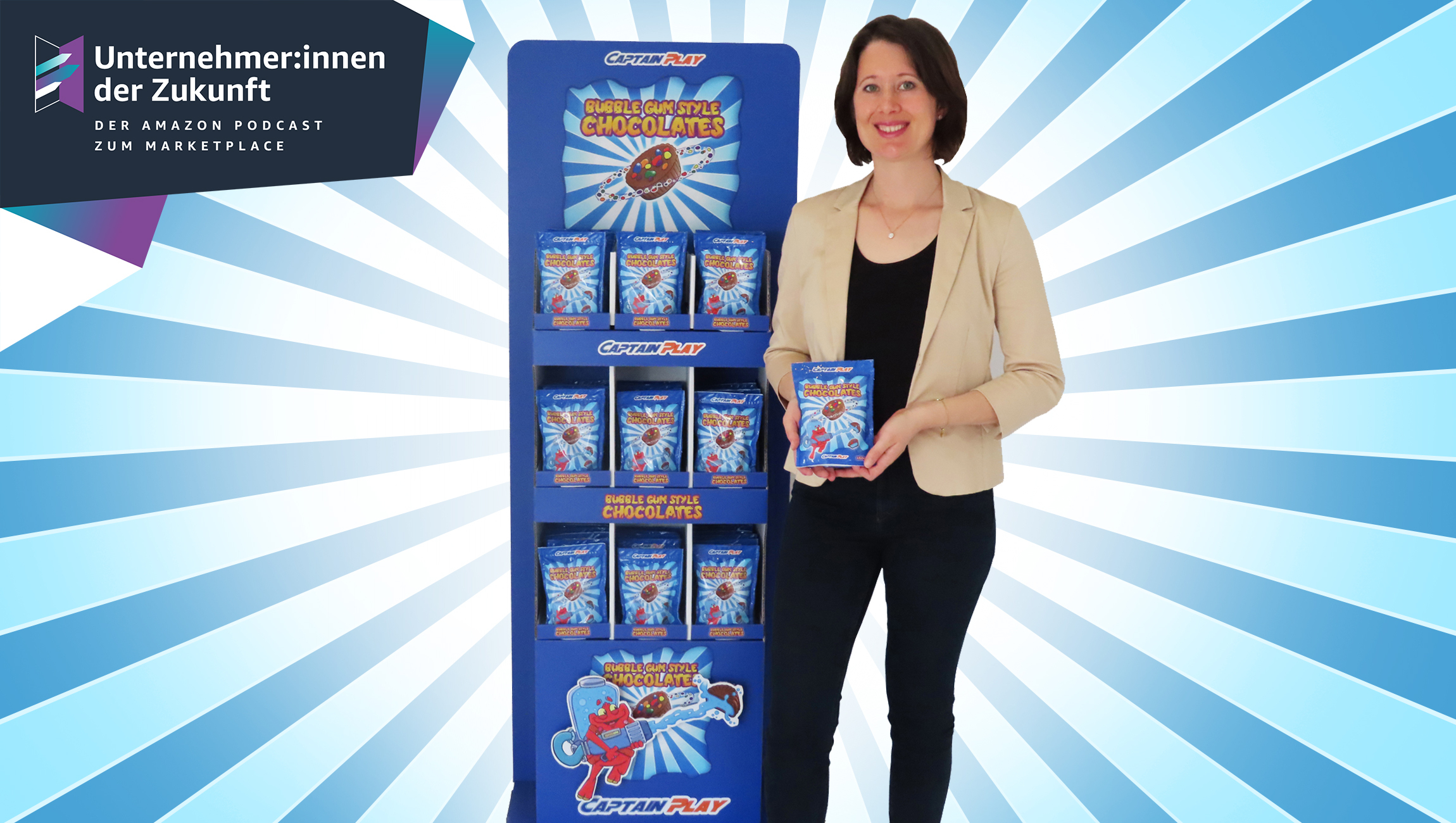 Annika Würtenberger, Gründerin von Captain Play, steht neben einem Süßigkeitenregal und hält eine Tüte mit Süßigkeiten in der Hand. Sie hat halblange braune Haare und lächelt in die Kamera. Sie trägt eine schwarze Hose, schwarzes Shirt und einen beigen Blazer.