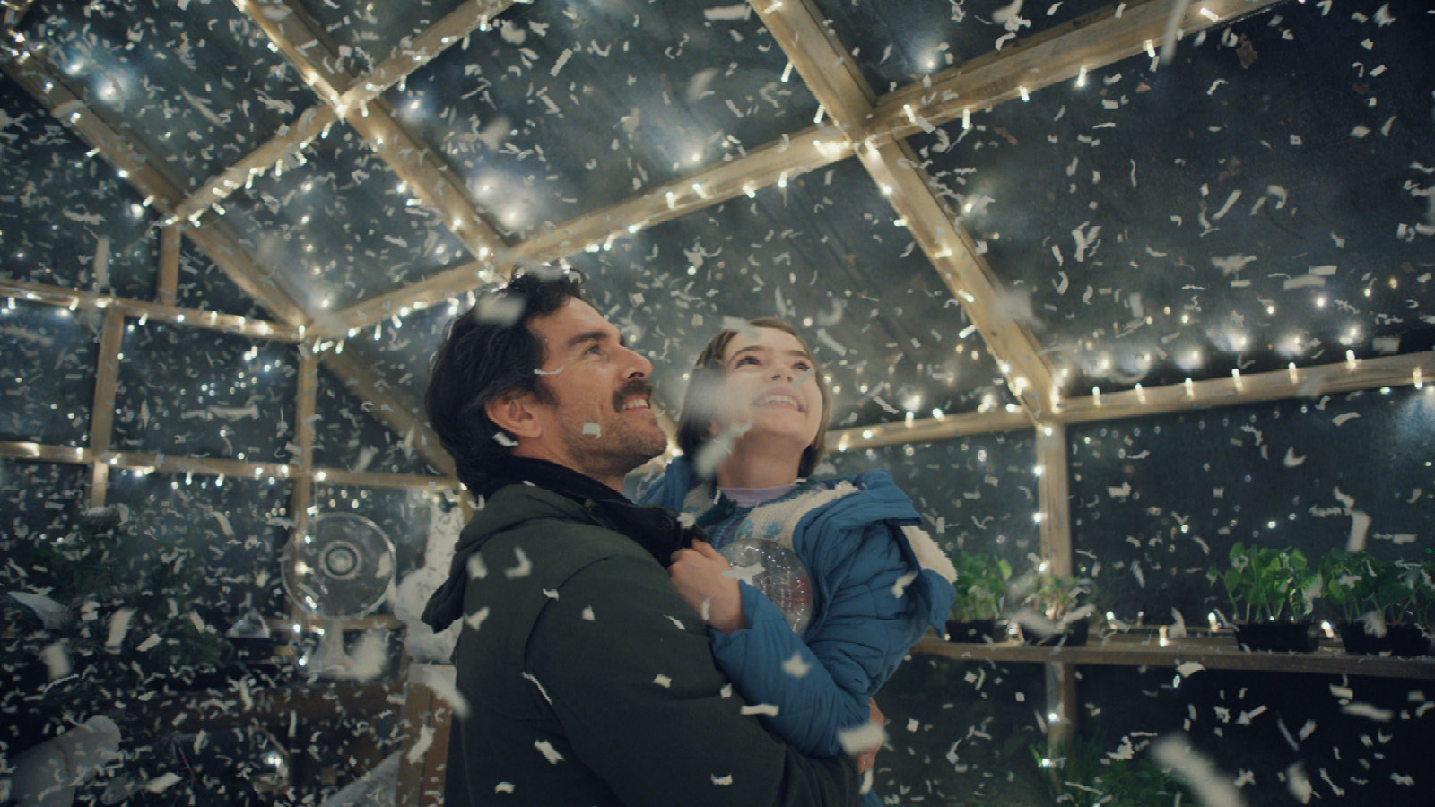 A father holds his daughter in his arms as they smile and stand in the homemade snowglobe.